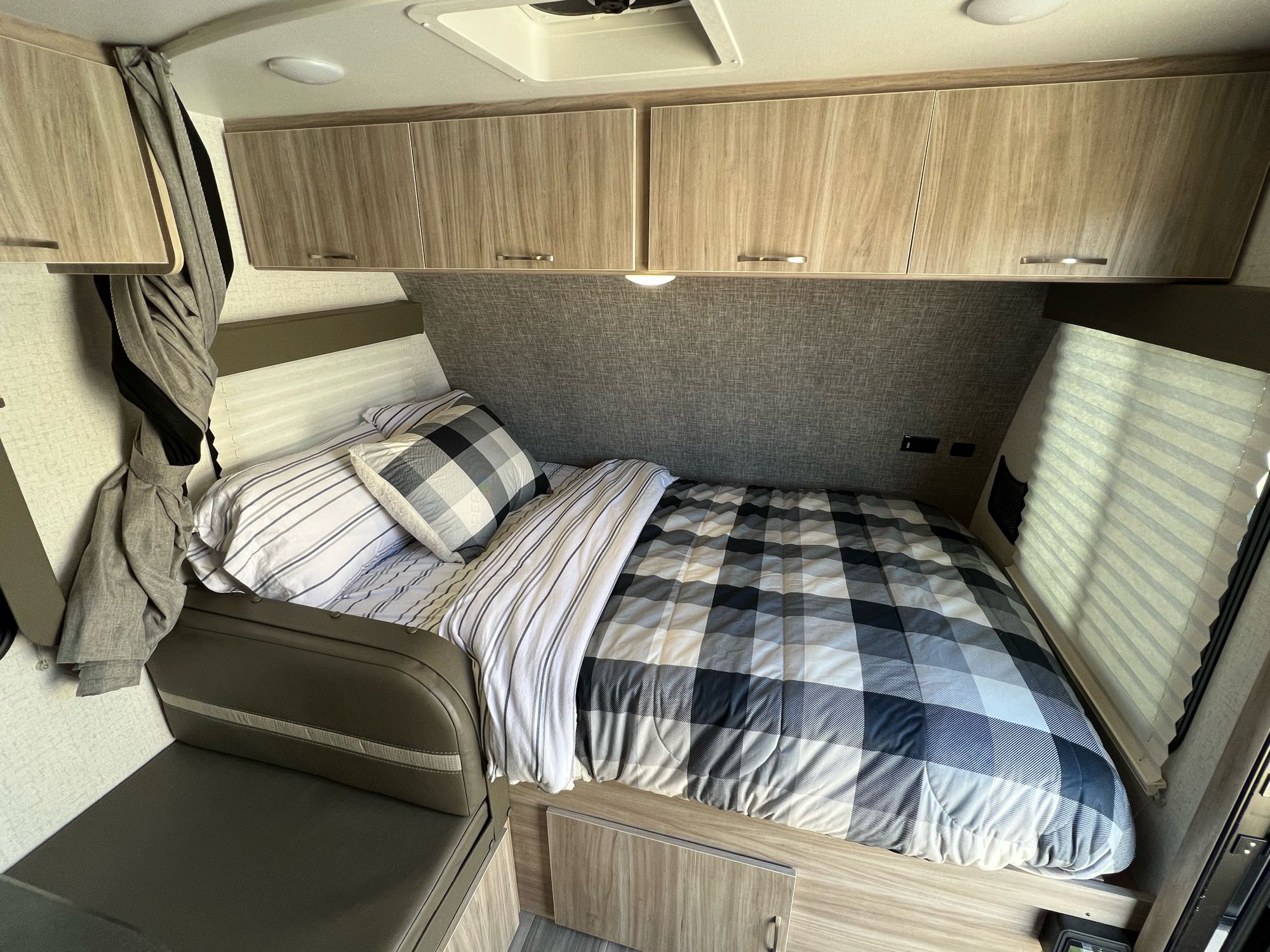 An RV rental's compact bedroom with striped and plaid bedding, overhead cabinets, and a side bench.. Winnebago Micro Minnie 2022
