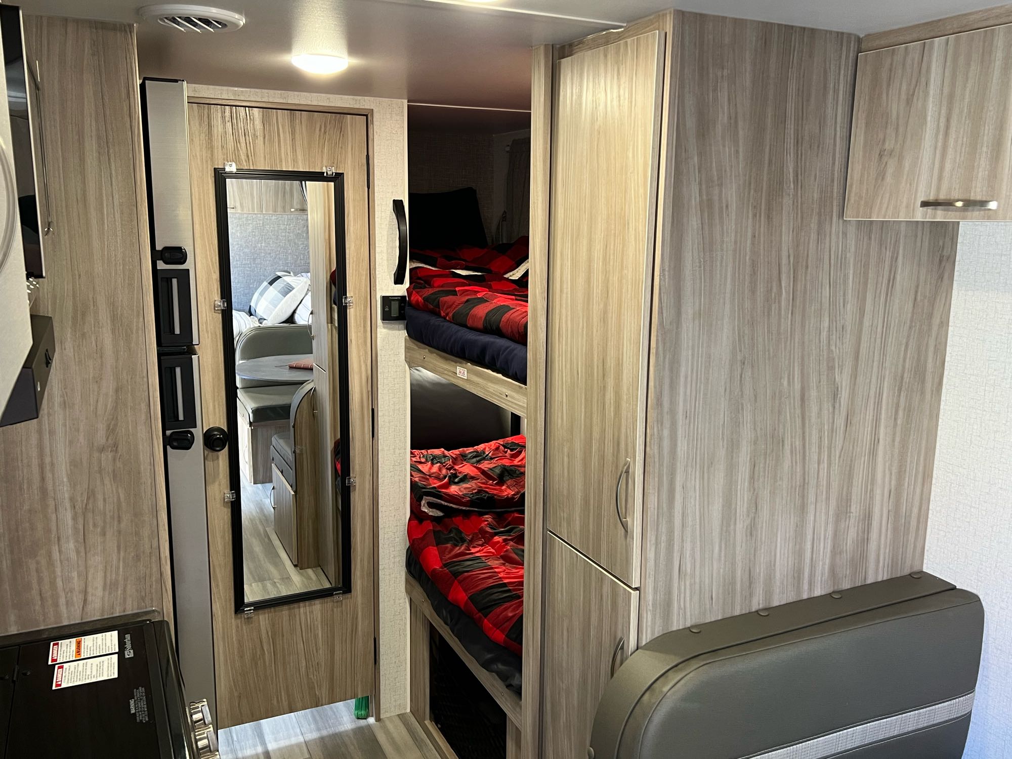 Inside this **RV rental**: cozy bunk beds with plaid blankets, a mirrored door, and light wood interior finishes.. Winnebago Micro Minnie 2022