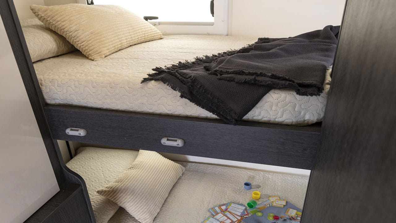 Cozy RV rental bunk beds with quilted bedding and games on the lower bunk. Ideal for family travel.. Roller Team Kronos 271 M 2022