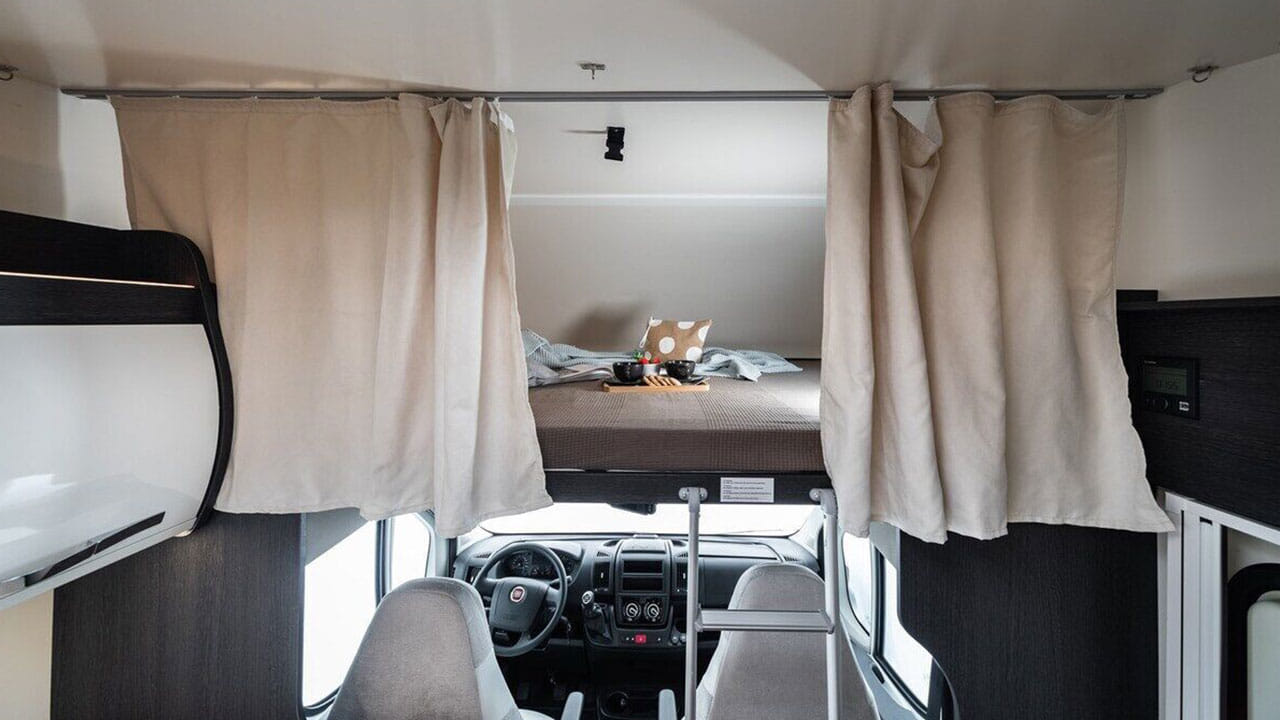 View inside an RV rental showing the over-cab bed with privacy curtains above the driver's cockpit.. Roller Team Kronos 271 M 2022