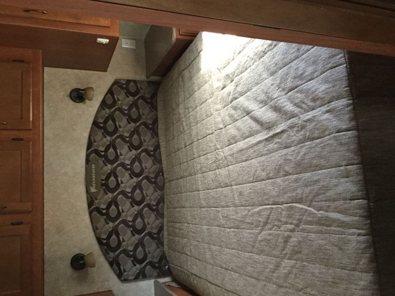 RV rental bedroom view: patterned headboard, light mattress, wood cabinets, and wall lights provide comfort.. Adventurer 31DS 2014