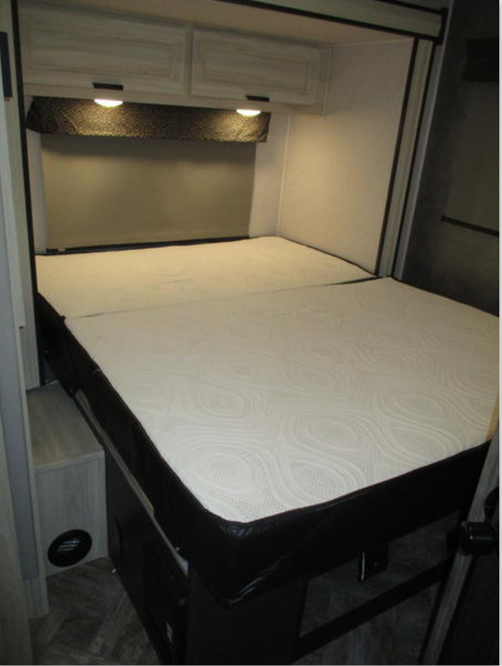 Cozy RV rental bedroom: a comfortable white mattress, overhead cabinets with lights, & a pull-down blind. Perfect for travel.. Forest River Sunseeker LE 2021