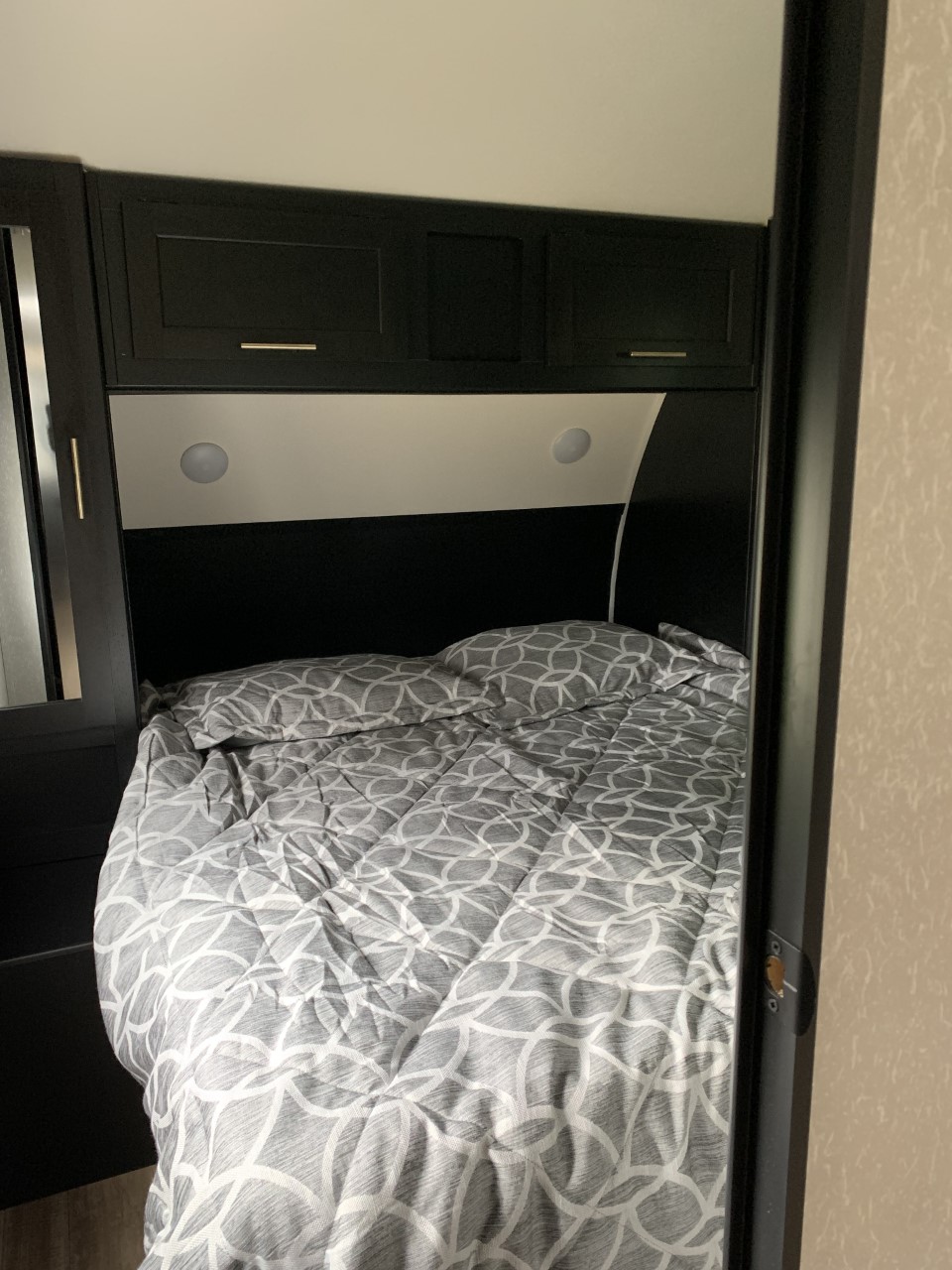 RV rental bedroom: Gray patterned bedding, dark overhead cabinets, and recessed lights provide a cozy sleeping space.. Forest River Cherokee 2022