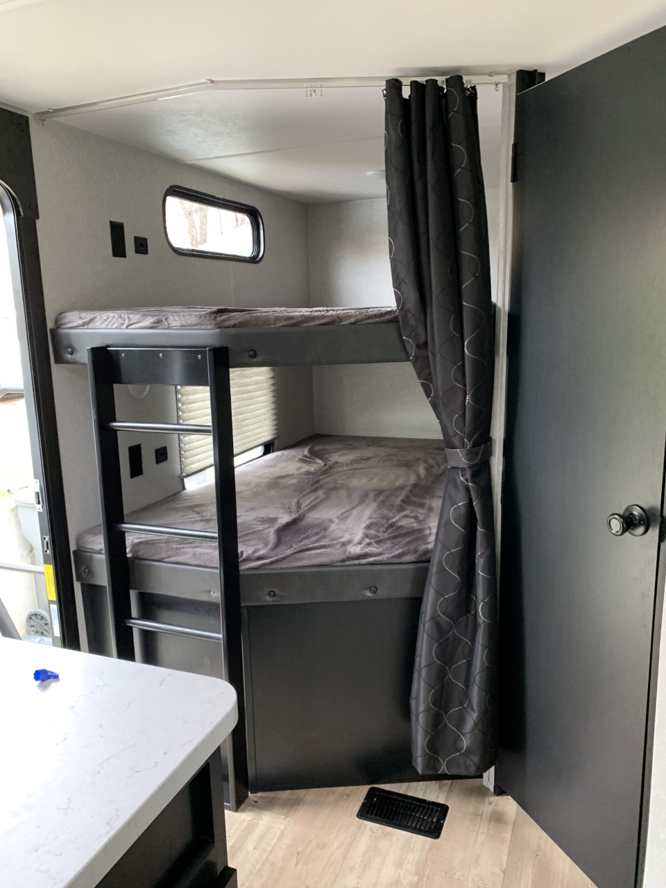Cozy bunk beds in an RV rental, with dark bedding, privacy curtain, ladder, and a small window for natural light.. Forest River Cherokee 2022