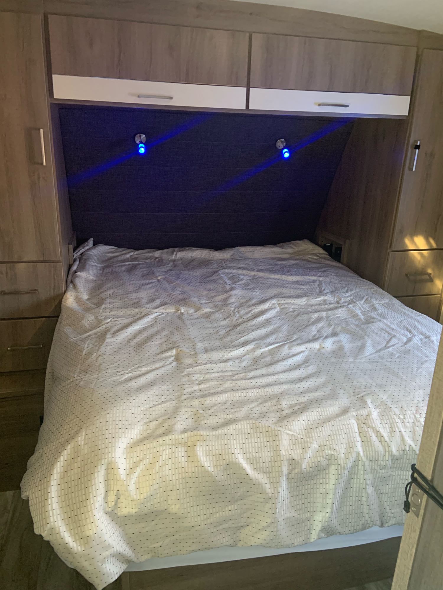 An RV rental bedroom features a bed with white patterned bedding, built-in wooden cabinets, and blue headboard lights.. Grand Design 2800BH 2021