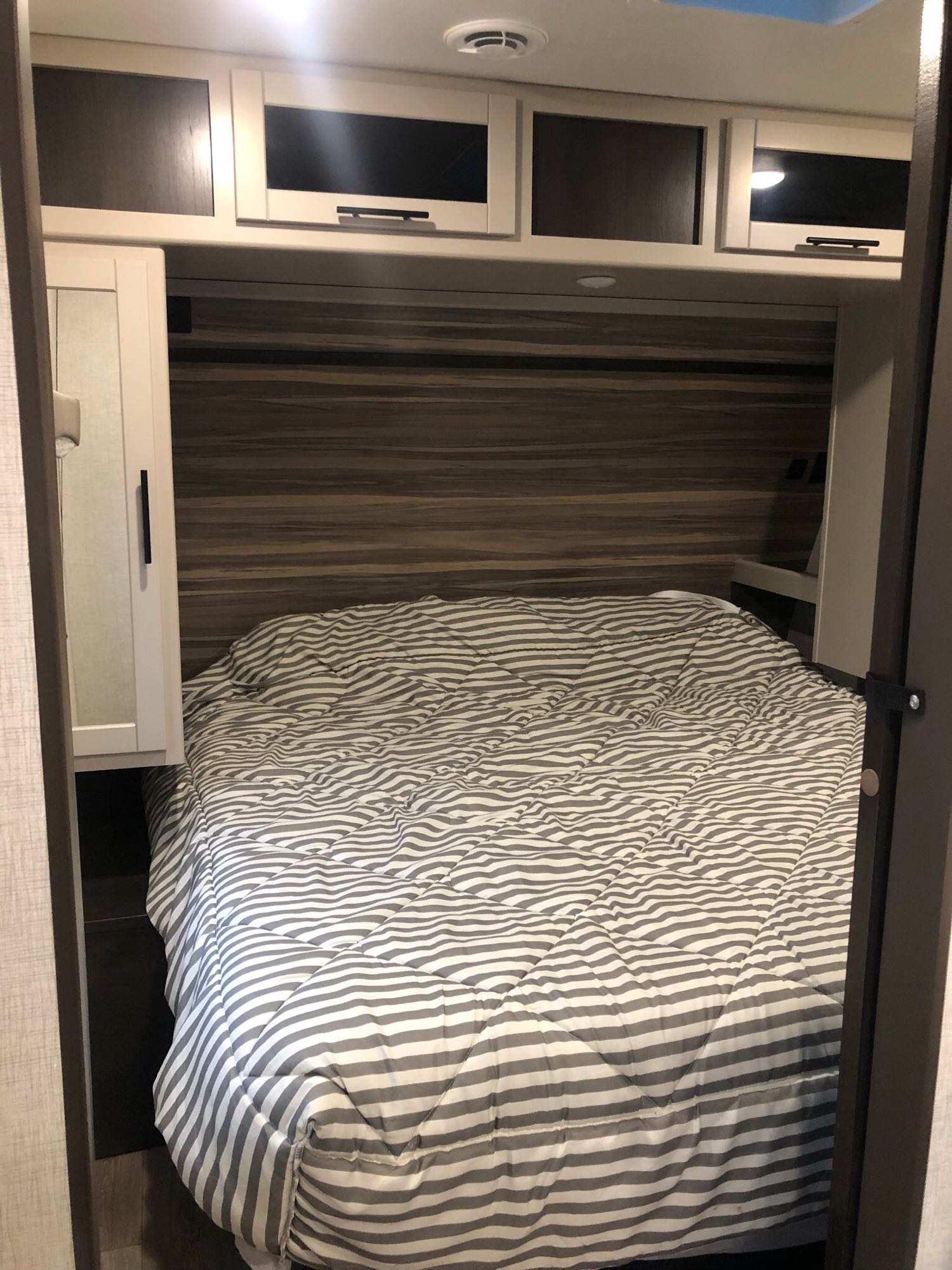 RV rental bedroom: cozy bed with striped comforter, overhead cabinets, and compact built-in storage.. Crossroads Cruiser Aire 2021