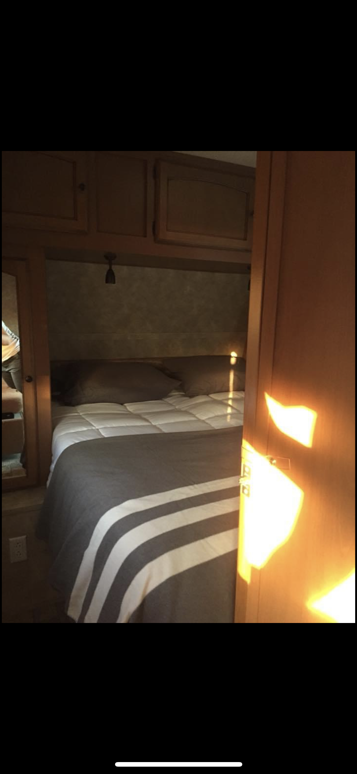 RV rental bedroom: cozy sleeping area with a striped comforter, overhead cabinets, and bright sunlight.. Gulf Stream Ultra-Lite 2014