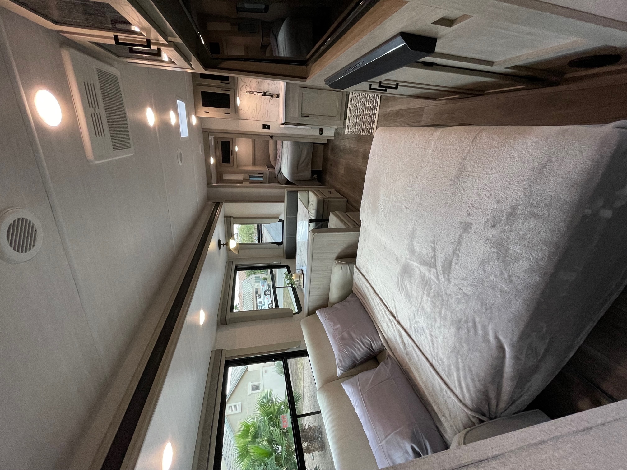 Inside a stylish RV rental: a cozy bed, living area with large windows, and full kitchen.. East to West Alta 2022