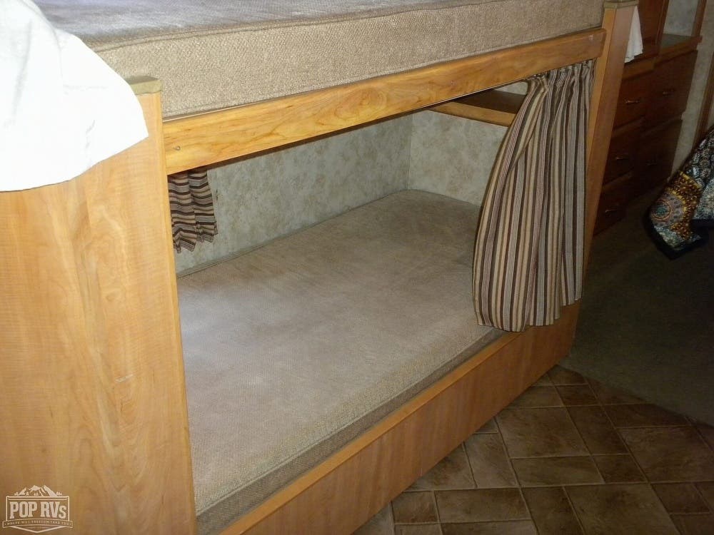 Comfortable RV rental bunk beds, perfect for family travel. Features wood frame, lower mattress, and privacy curtain.. Winnebago Access 2010