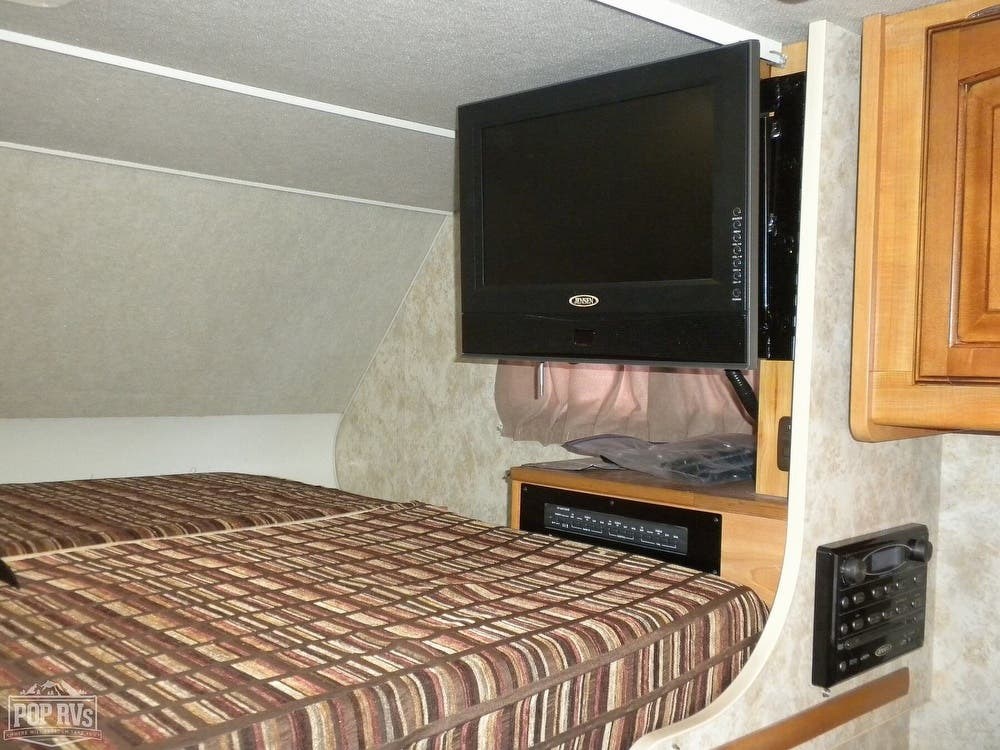 RV rental's sleeping area: a patterned bed, mounted Jensen TV, and entertainment system. Ready for travel.. Winnebago Access 2010