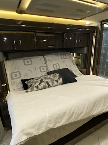 Modern RV bedroom featuring a large, comfortable bed with patterned headboard cushions and overhead storage. Ideal for an RV rental.. American Coach American Heritage 45e 2020