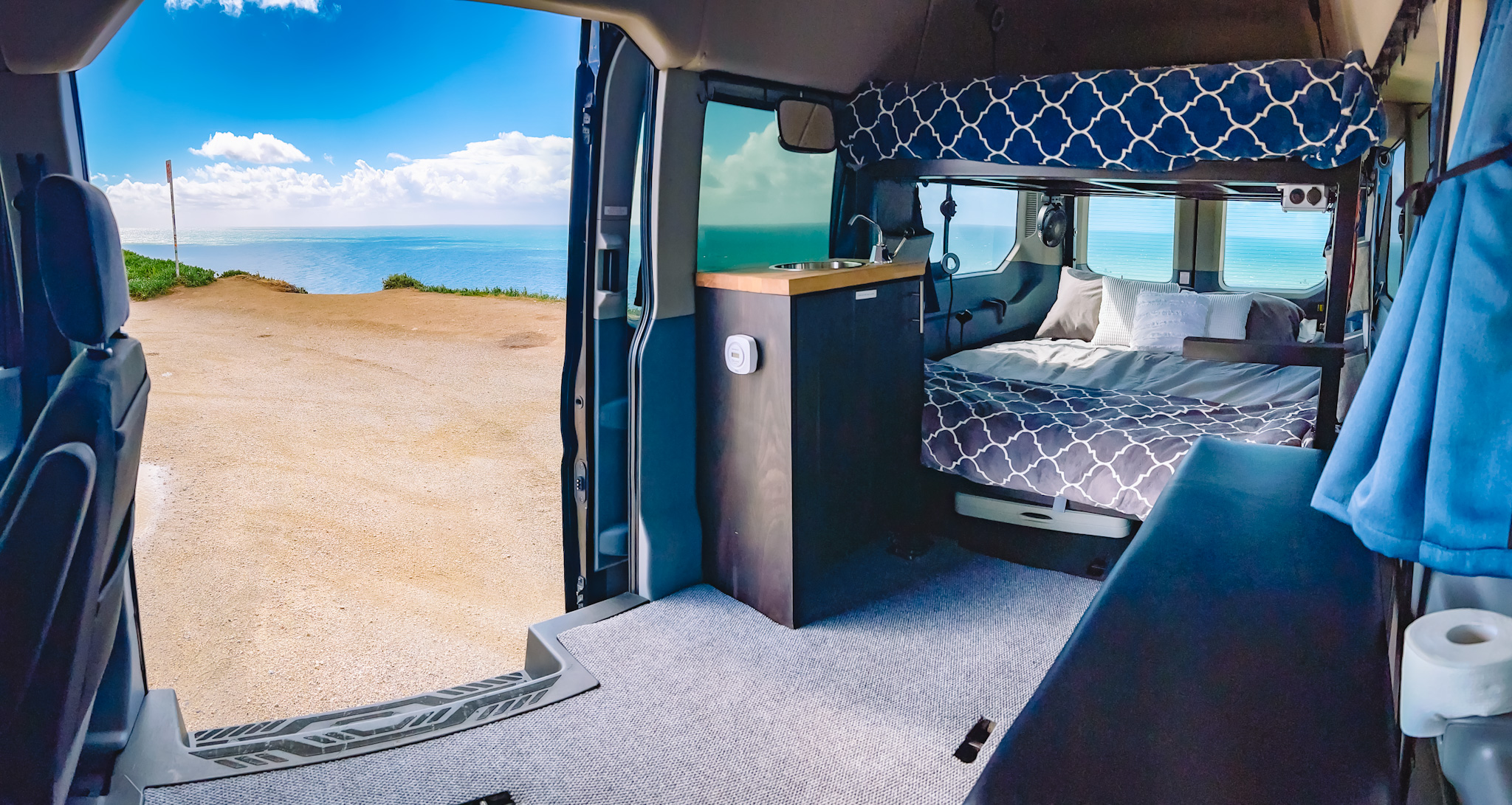 Spacious RV rental campervan interior with bed, kitchen, & an open door revealing a stunning ocean view.. Ford Transit Custom 2019