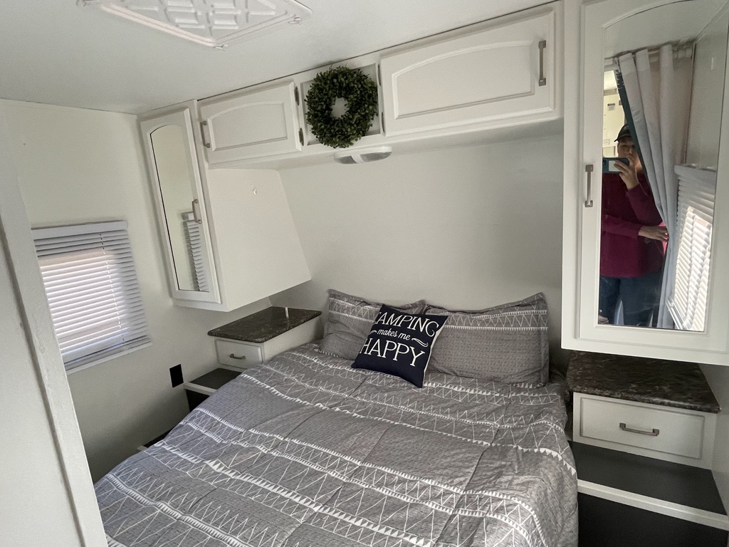 Inside an RV rental, this cozy bedroom features gray bedding, white overhead cabinets, a wreath, and a mirrored wardrobe.. Keystone RV Springdale 2015