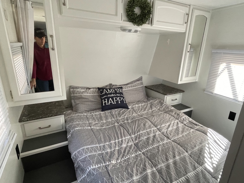 Inviting RV rental bedroom: white cabinets, patterned bedding, "Camping makes me HAPPY" pillow, & mirror reflection.. Keystone RV Springdale 2015