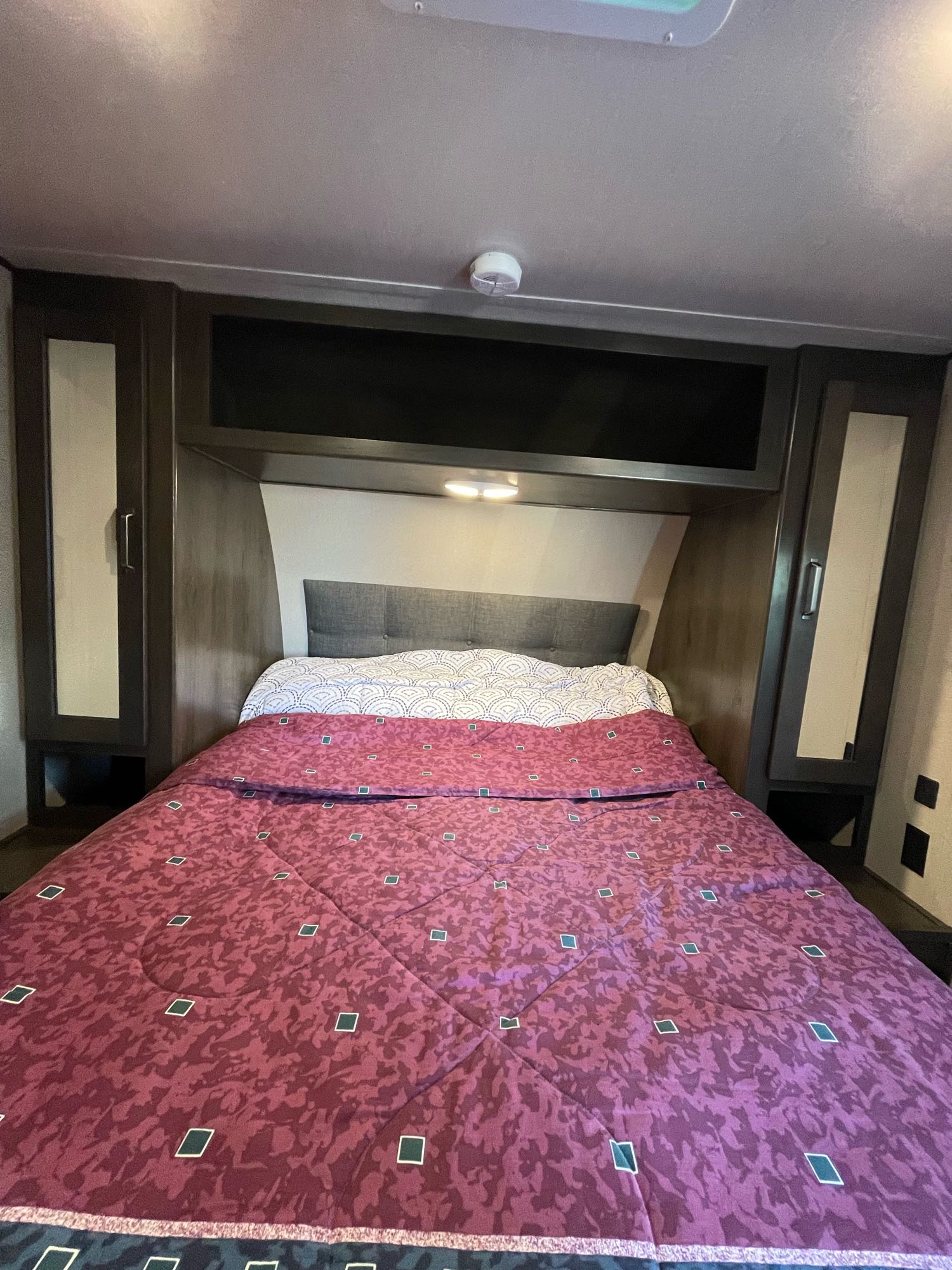 Compact bedroom in an RV rental featuring a comfortable bed, mirrored wardrobes, and overhead storage for travel.. Grand Design Transcend Xplor 2021