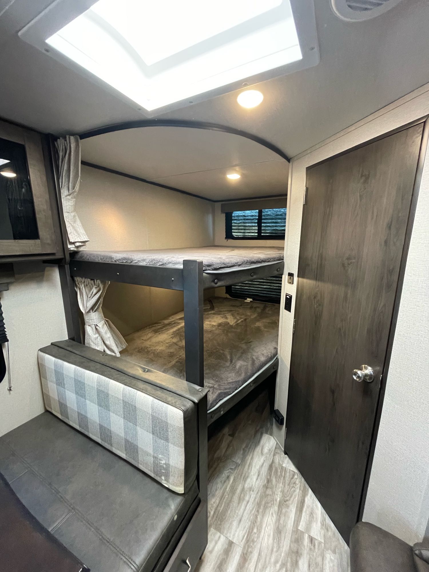 This cozy RV rental interior features stacked bunk beds, a plaid dinette, and bright lighting, ideal for family travel.. Grand Design Transcend Xplor 2021
