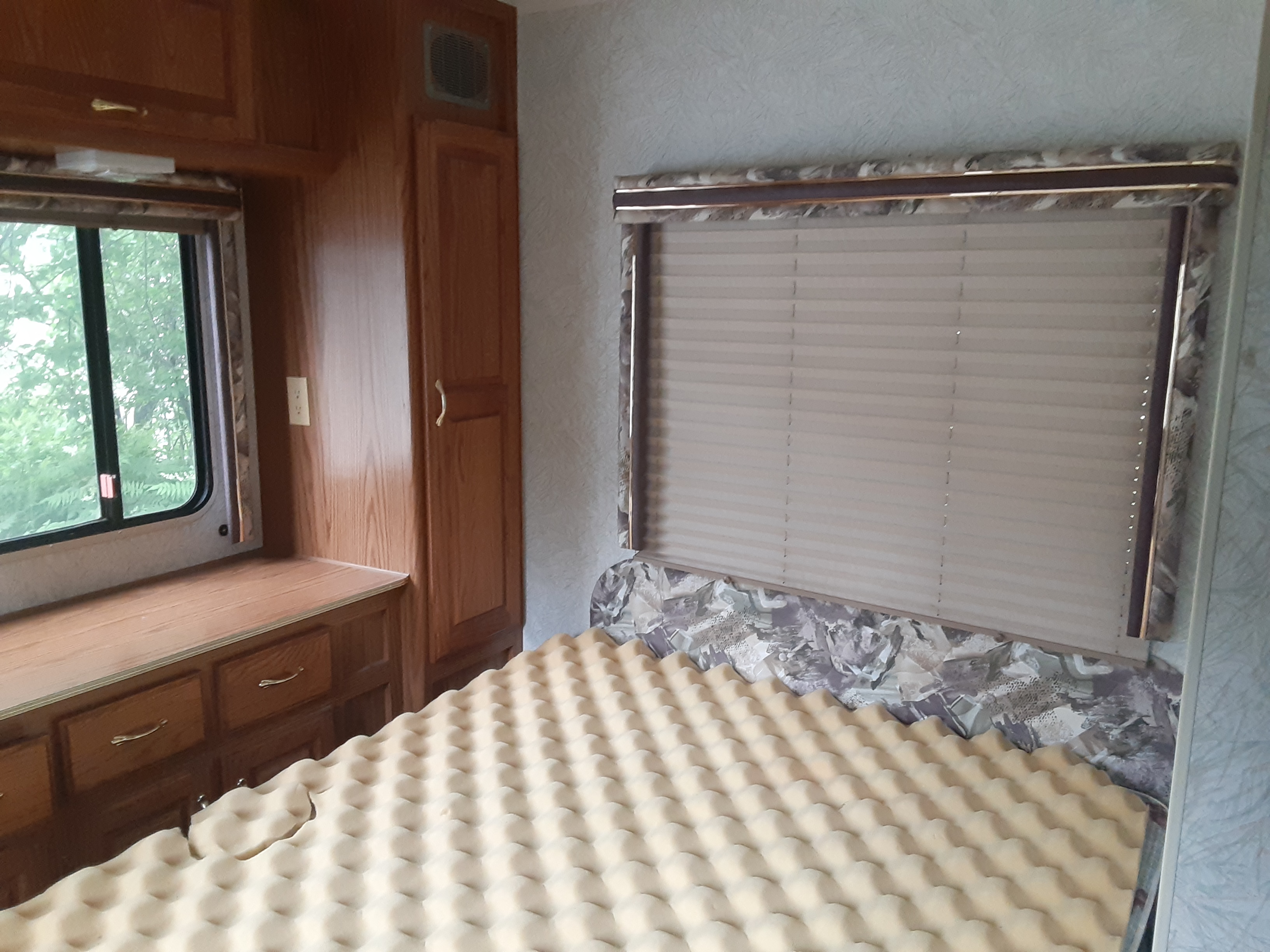 Cozy RV rental bedroom featuring wood cabinets, a window with outdoor views, and a bed with a foam topper & patterned headboard.. Jayco Eagle 1996