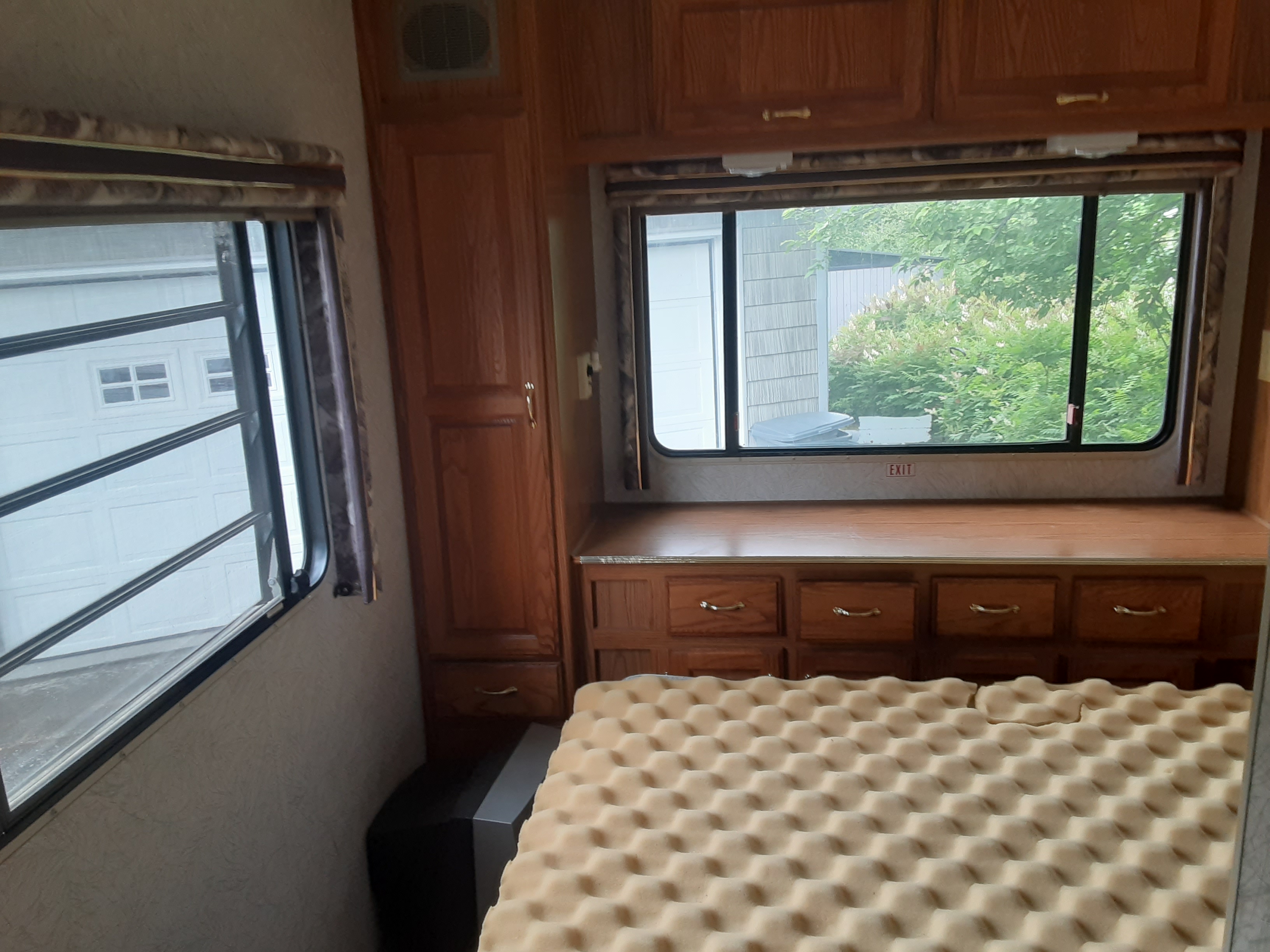 Cozy RV rental bedroom with foam mattress, wooden cabinets, and windows offering views of outside. Ideal for travel accommodation.. Jayco Eagle 1996