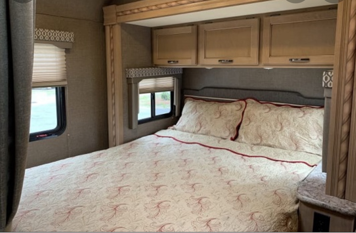 Cozy RV rental bedroom with patterned bedding, overhead cabinets, and windows, offering comfortable accommodations for travel.. Thor Freedom Elite 2018
