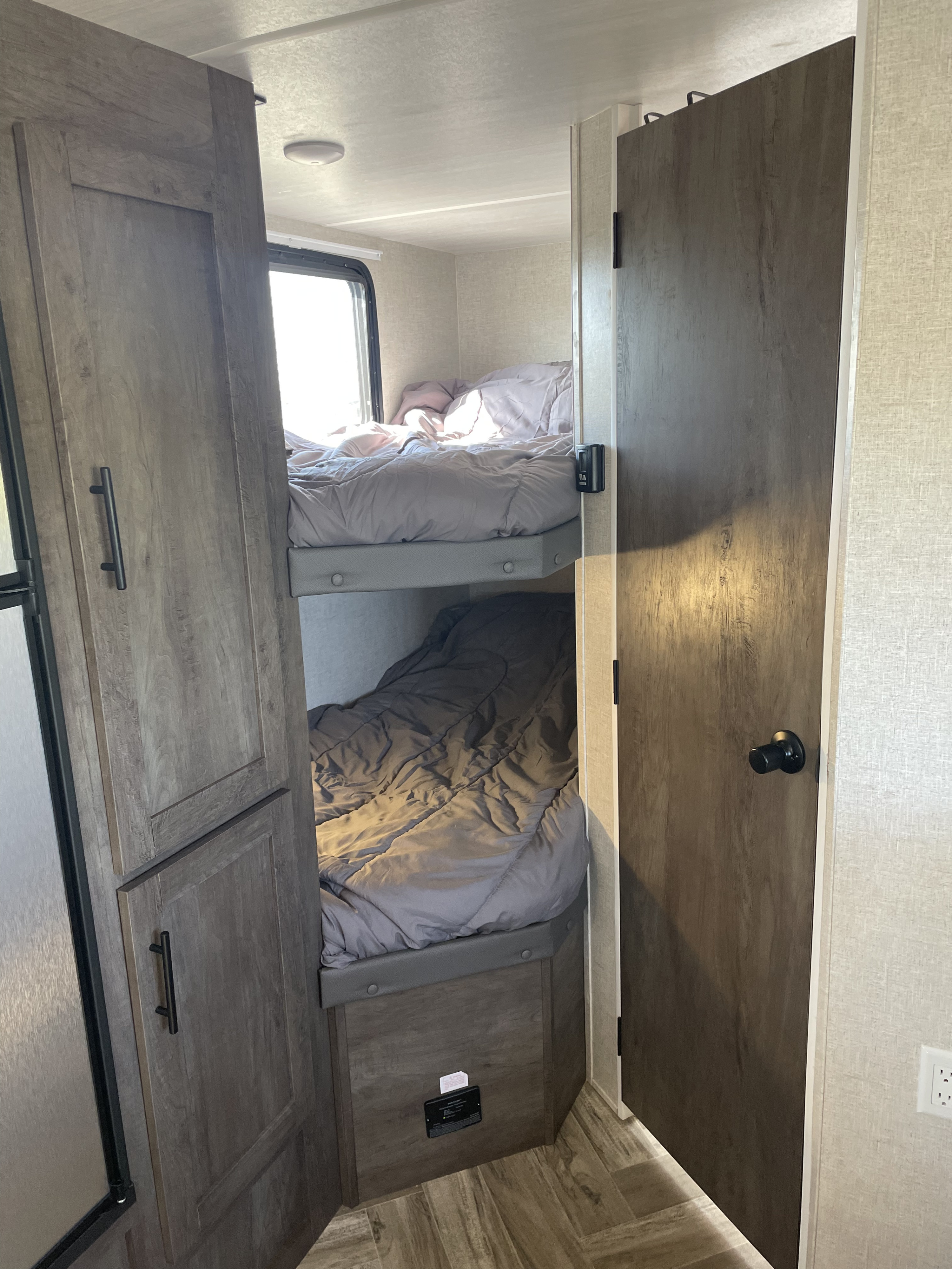 Cozy rv rental interior featuring comfortable bunk beds with gray bedding, built-in cabinetry, and a compact sleeping nook.. Forest River EVO 2021