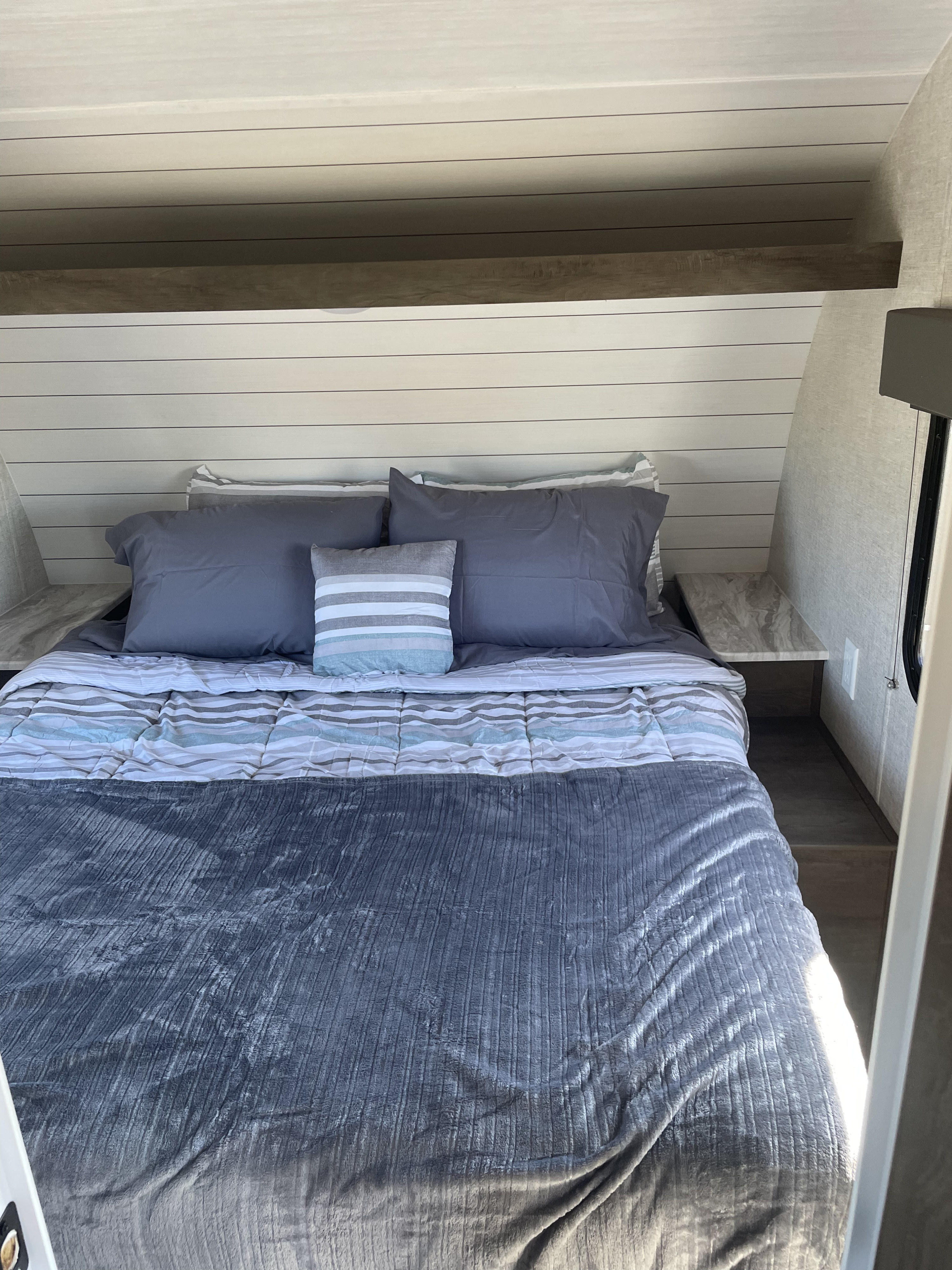 RV rental interior: A cozy bedroom with gray and white striped bedding, a shiplap headboard, and side storage.. Forest River EVO 2021