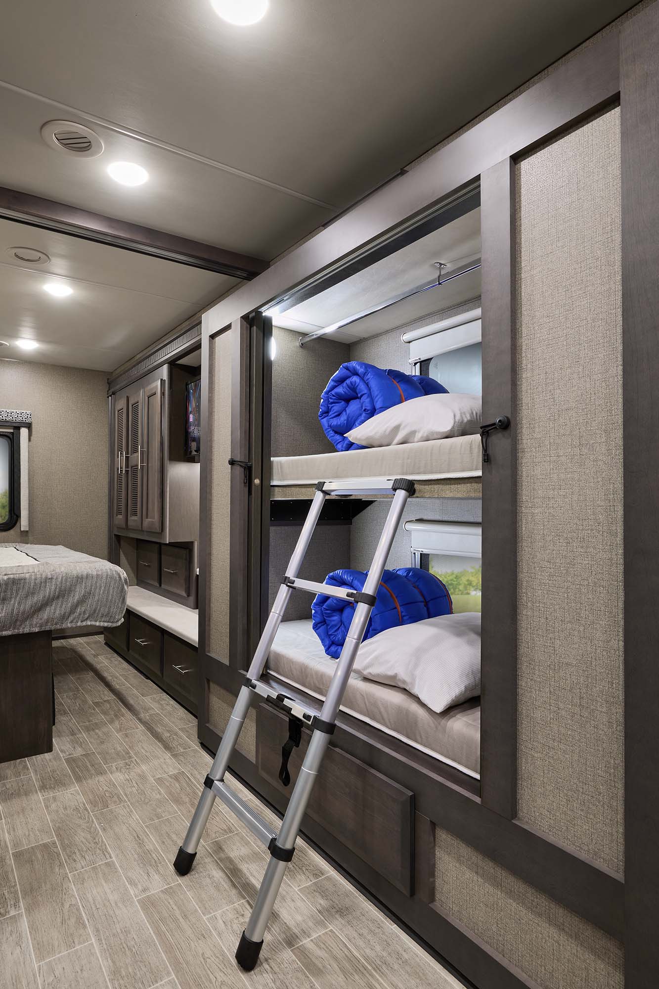 This RV rental interior features two bunk beds with blue sleeping bags, a main bed, & built-in storage for comfortable travel.. Thor Omni RS36 2022