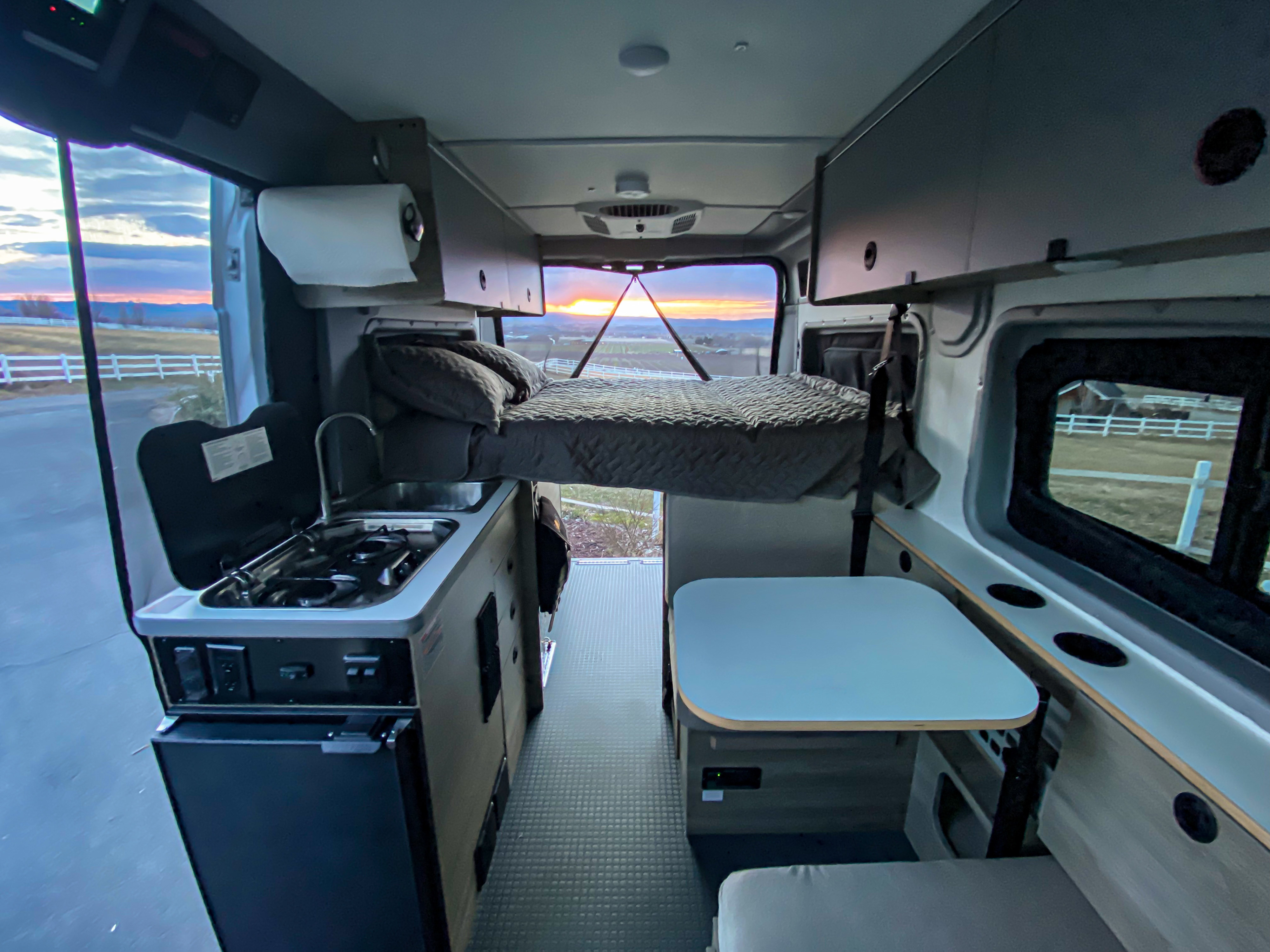 Inside a spacious RV rental: full kitchen, elevated bed, and dining area with a beautiful sunset view from the back.. Winnebago Solis Pocket 2022
