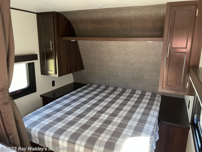 Inside an RV rental: a compact bedroom features a plaid bed, dark wood cabinets, and overhead storage.. Jayco Jay Flight 2020