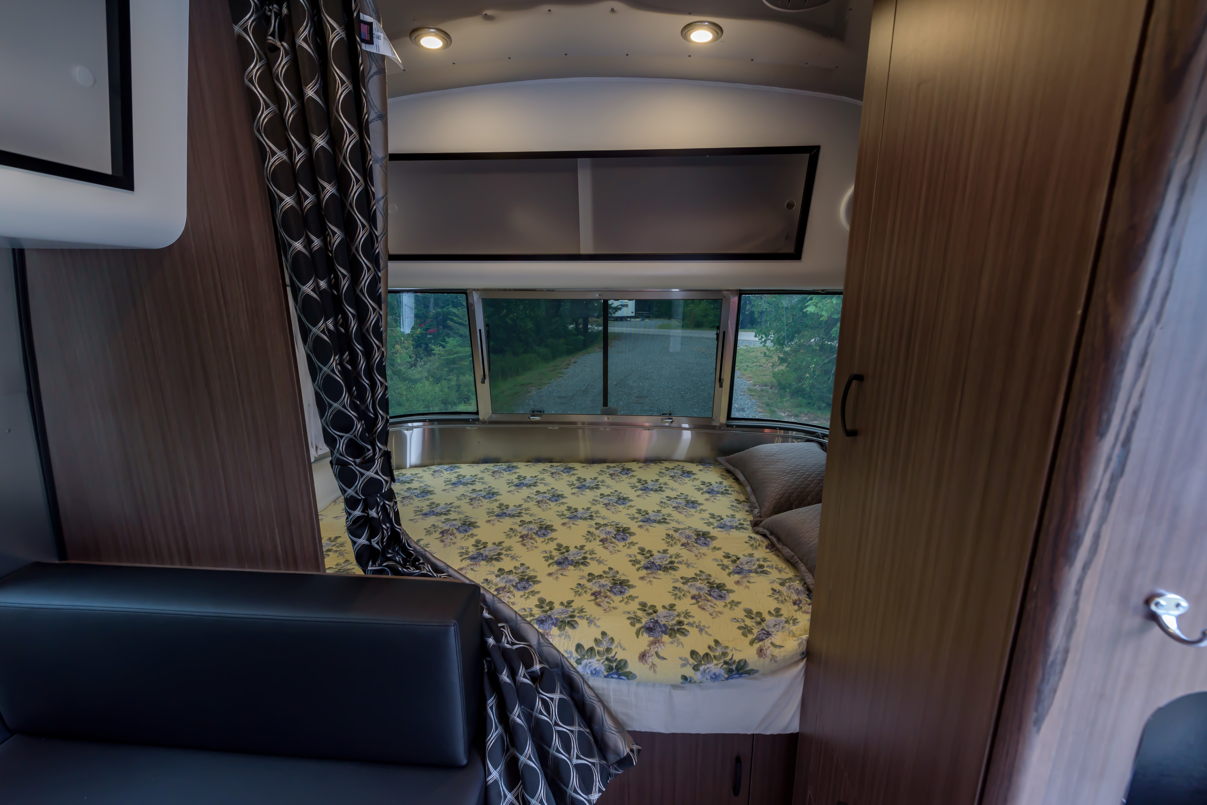 Bright Airstream-style RV rental interior: floral bed, black sofa, and large windows showcasing outdoor scenery.. Airstream Caravel 2022
