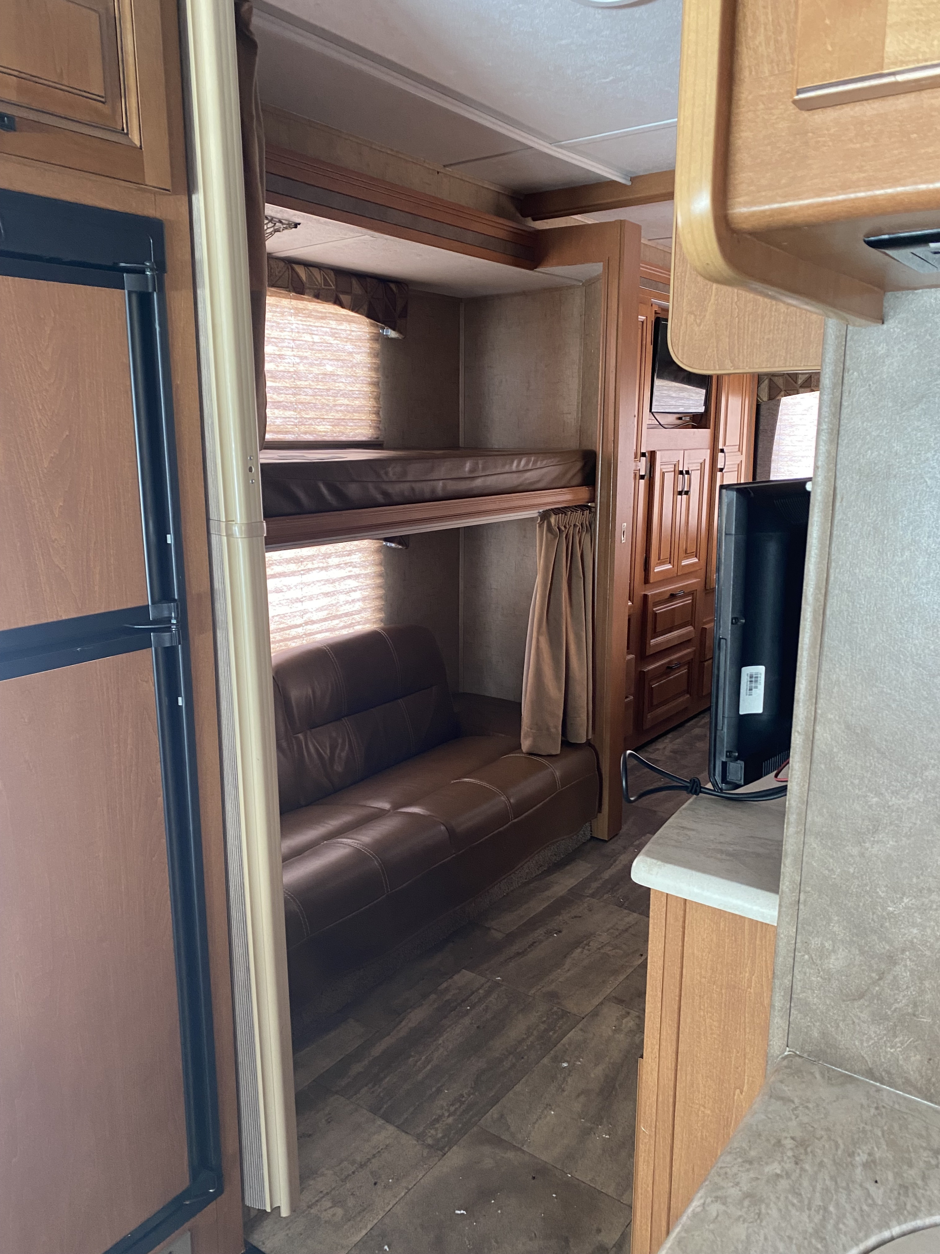 Explore this RV rental's interior: functional bunk beds, a comfy brown sofa, refrigerator, and TV area on wood-look flooring.. Forest River Sunseeker 2016