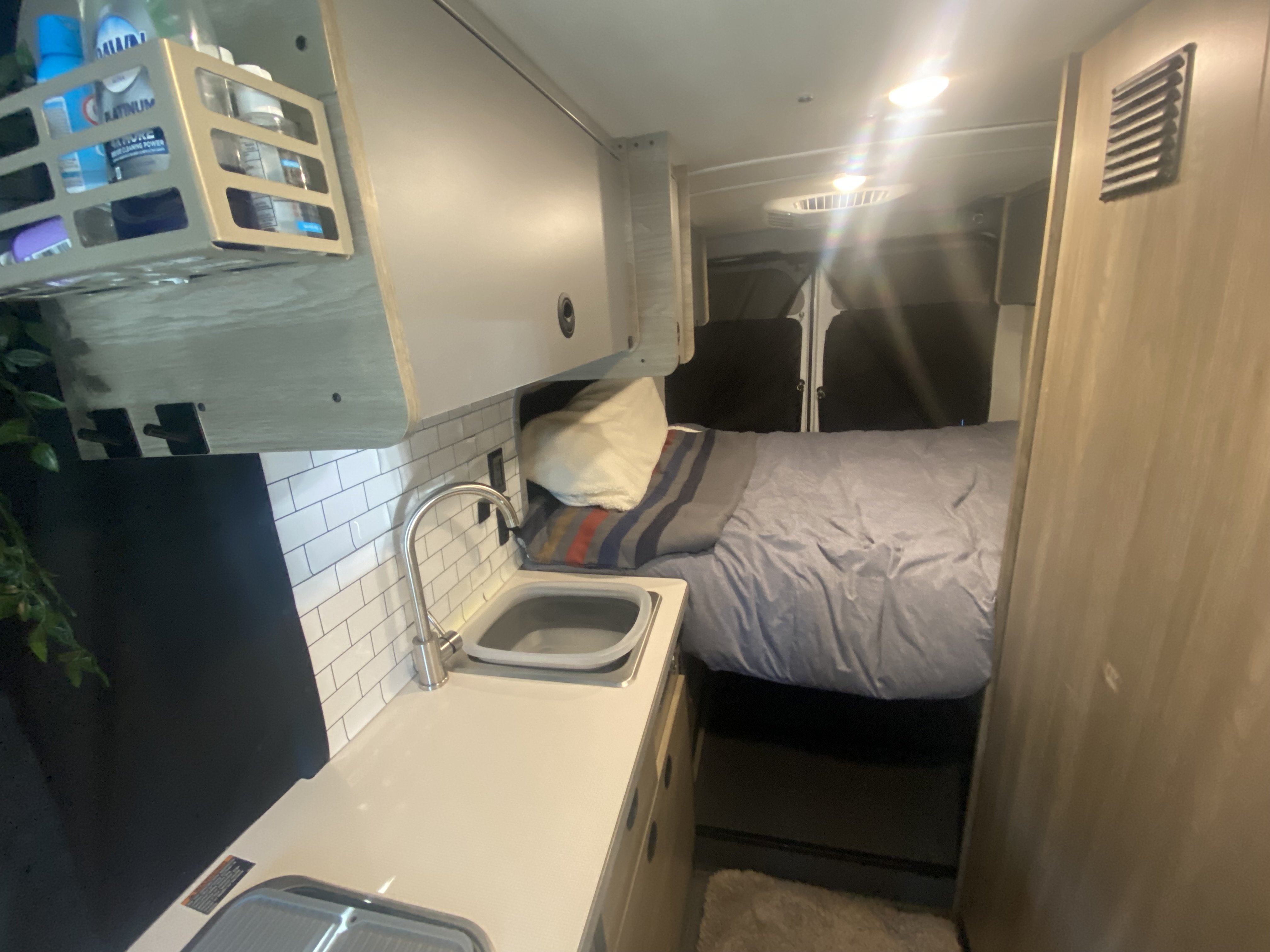 Inside this RV rental: a cozy bed, compact kitchenette with sink, and overhead storage. Ideal for road trips.. Winnebago Solis 2022