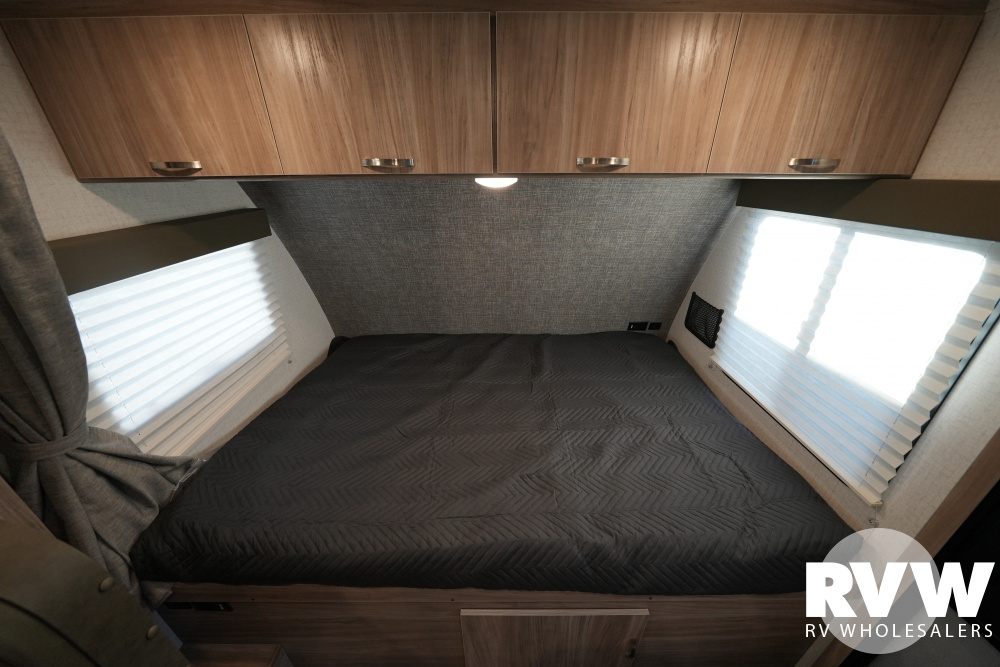 Cozy RV rental bedroom featuring a large bed with a dark comforter, overhead wood cabinets, and bright windows.. Winnebago Micro Minnie 2022