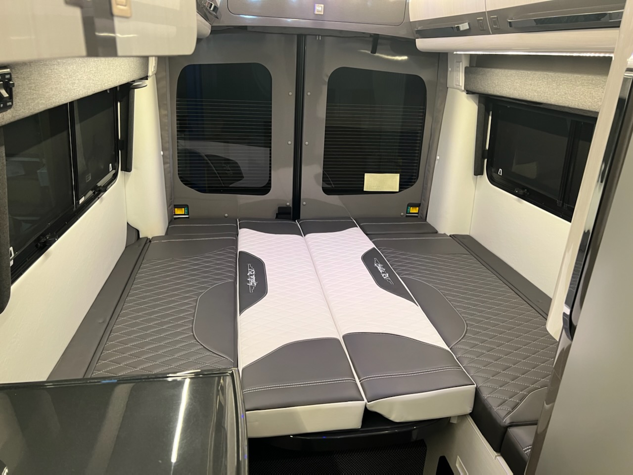 RV rental camper van interior: A cozy, modular bed setup with quilted grey and white cushions and windows.. Gala RV Monte Carlo 2100 LX 2022