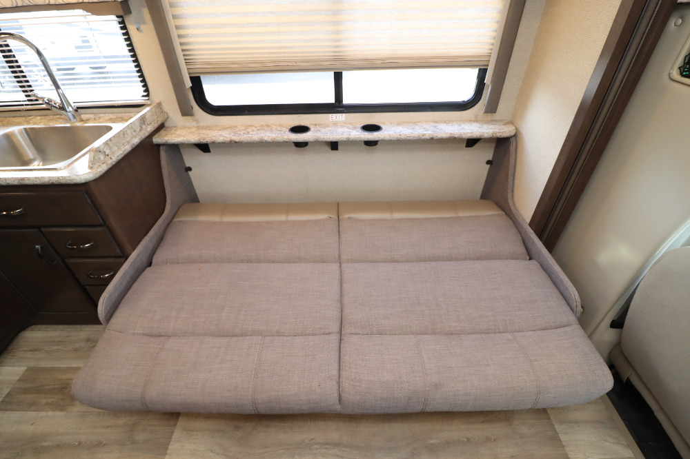RV rental interior with a versatile convertible sofa-bed, kitchen sink, and overhead shelf with cup holders by the window.. Thor Freedom Elite 2019