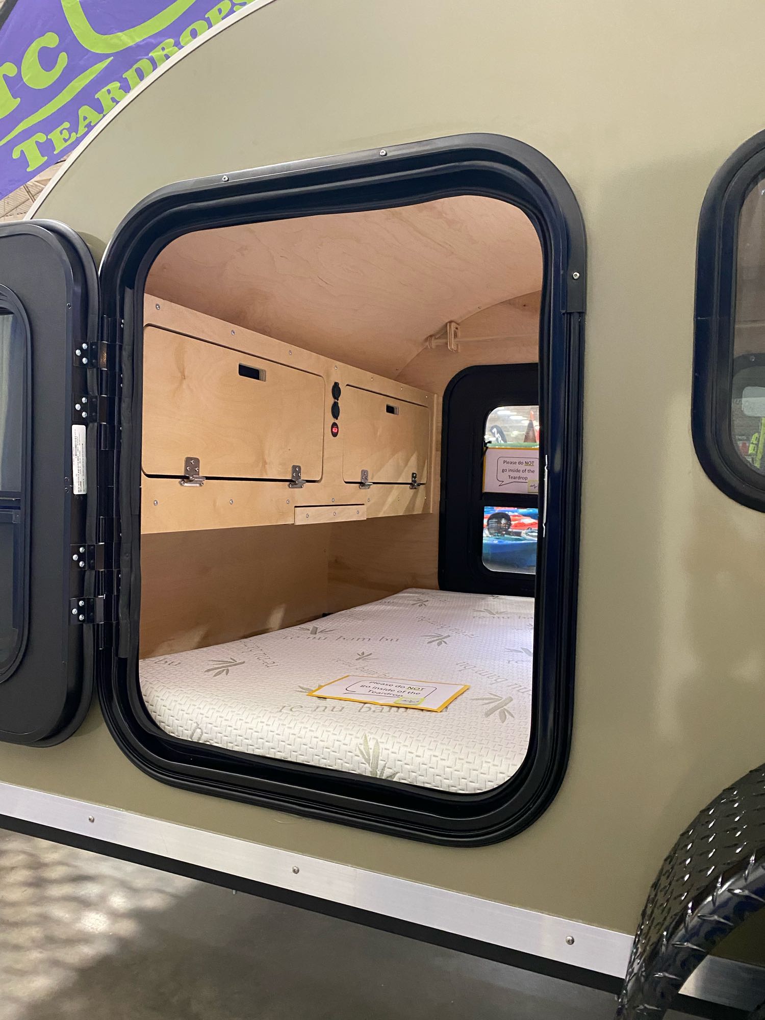 View inside a compact teardrop RV rental: a cozy mattress and wooden storage are visible through the open side door.. TC Tear Drop TC Original 2022