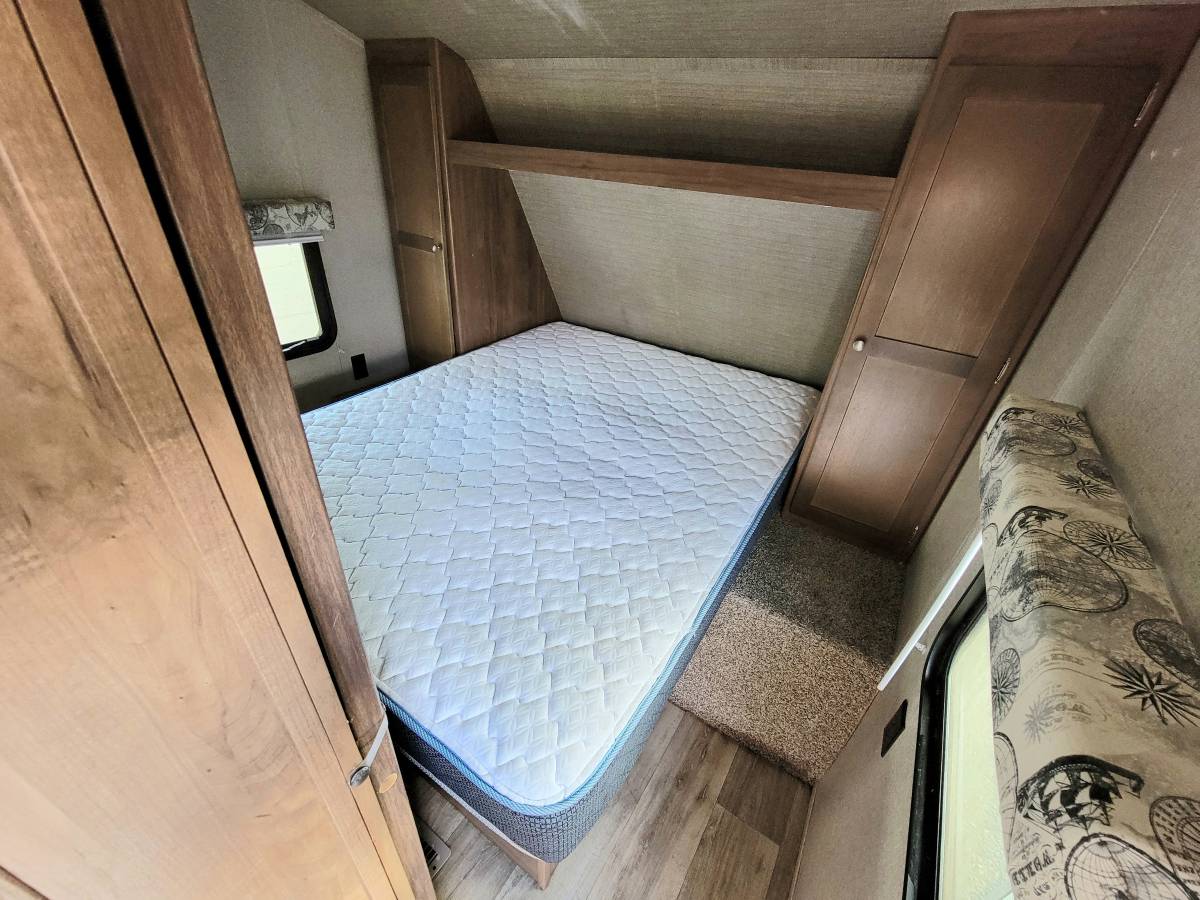 Inside an RV rental: a compact bedroom with a mattress, window, and wood storage cabinets on both sides of the bed.. Aspen Trail Aspen Trail Trailer 2018