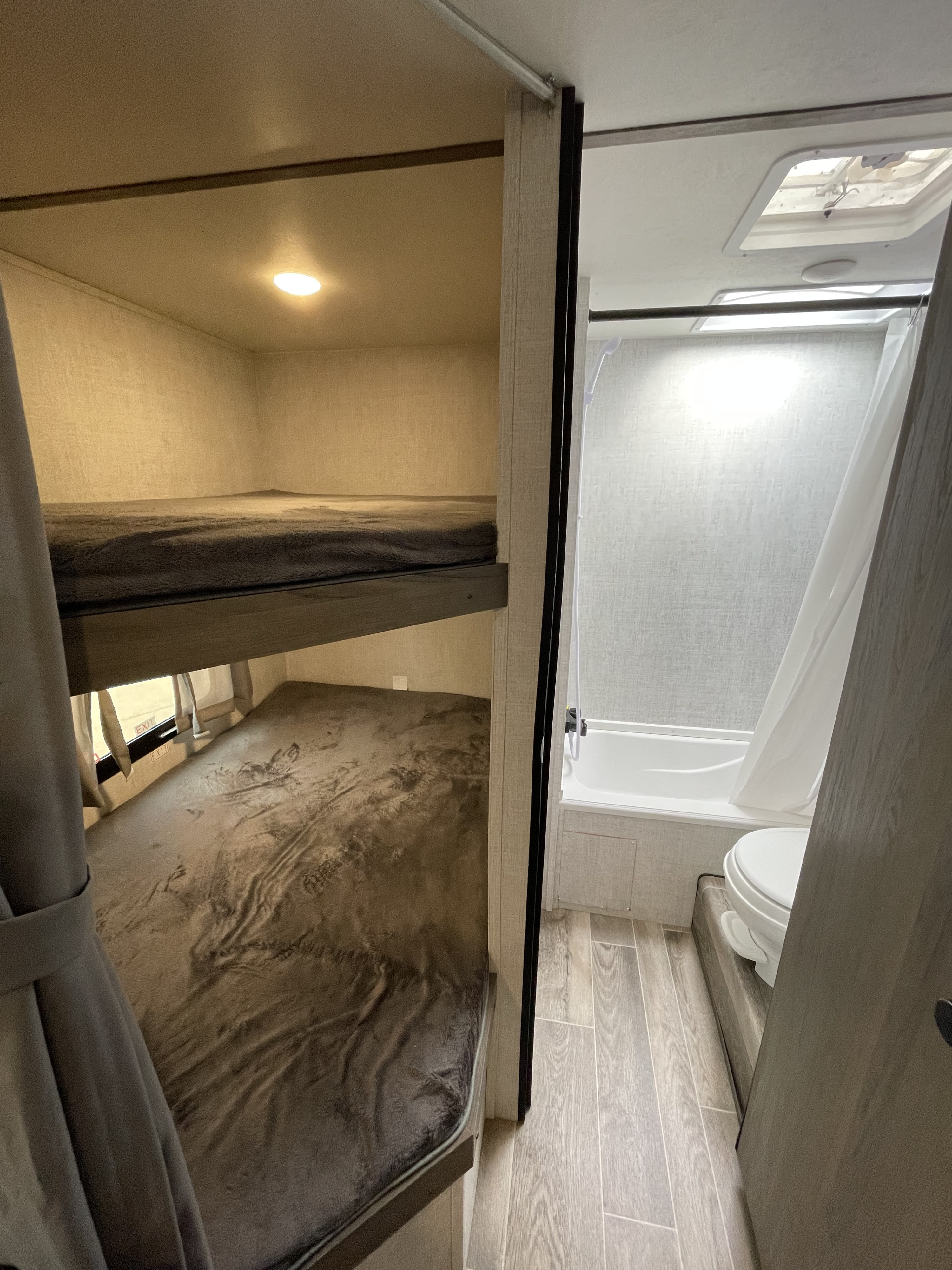 Inside an RV rental: cozy bunk beds on the left, and a compact bathroom with shower/tub and toilet on the right.. Gulf Stream Kingsport 2021