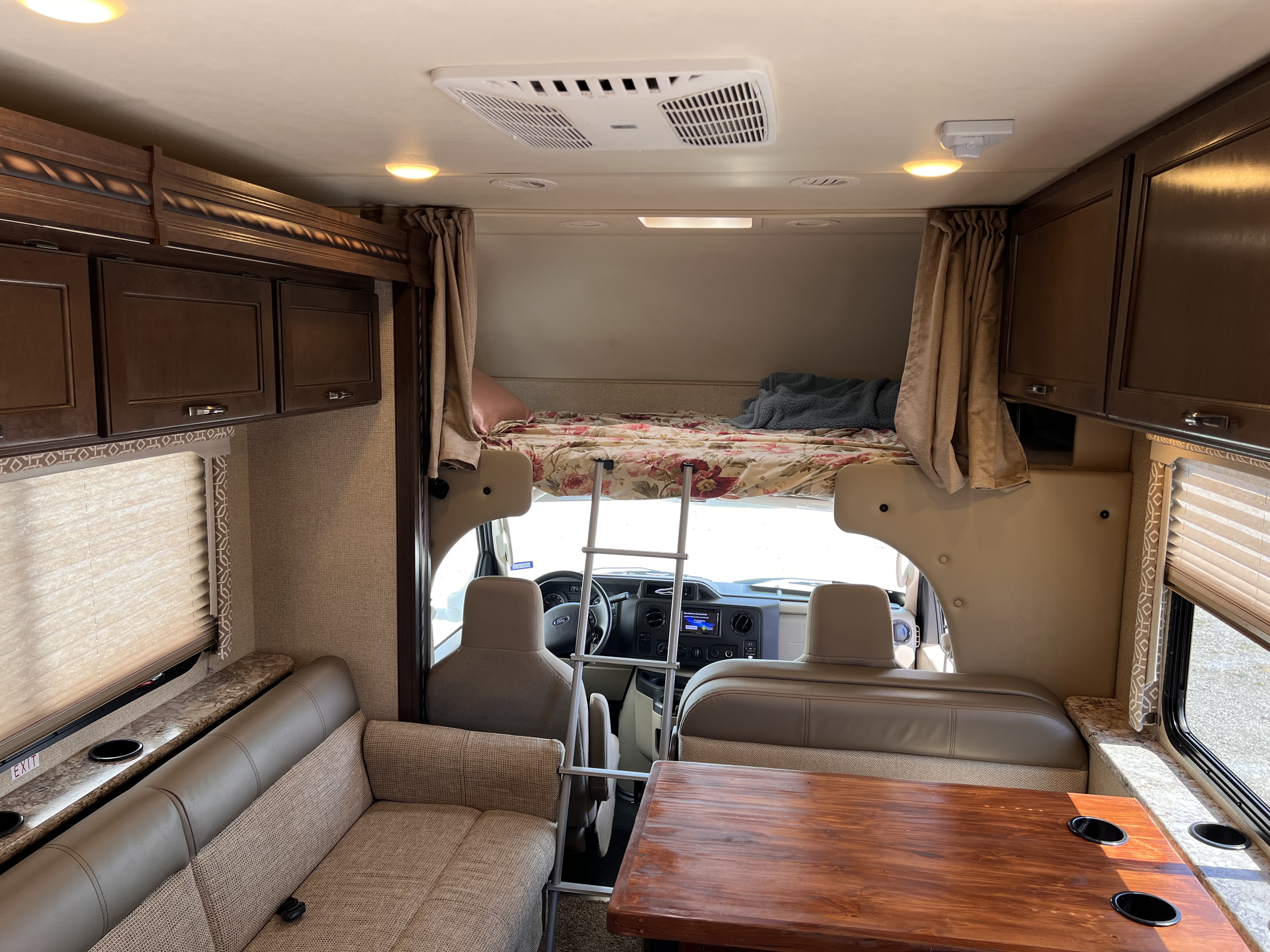 Inside an RV rental: view of the cozy living space with sofa, dining table, and overhead bunk. Ideal for family adventures.. Thor Freedom Elite 2017