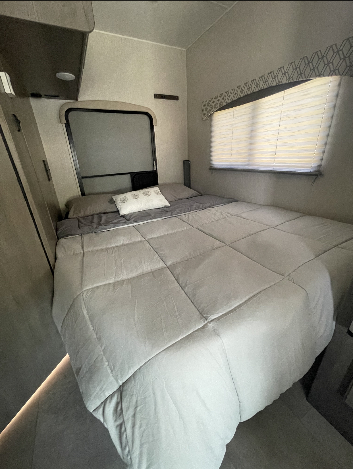 This cozy RV rental bedroom features a neatly made bed, window with blinds, and a small cabinet on the left.. Coachmen Freelander 2020