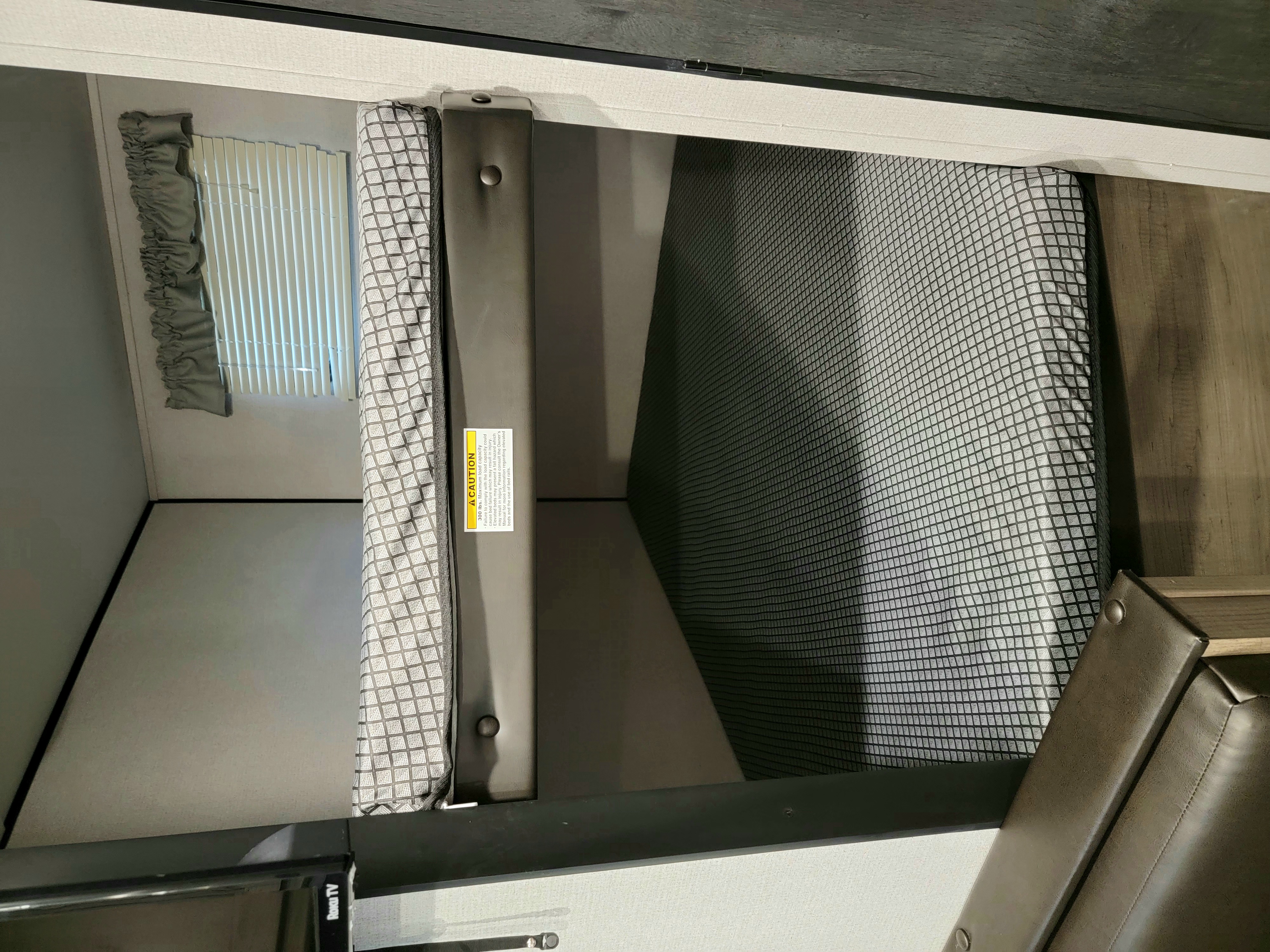 An RV rental bunk bed with safety netting and window. A caution label for elevated beds and a Roku TV are visible.. Keystone Hideout 2021