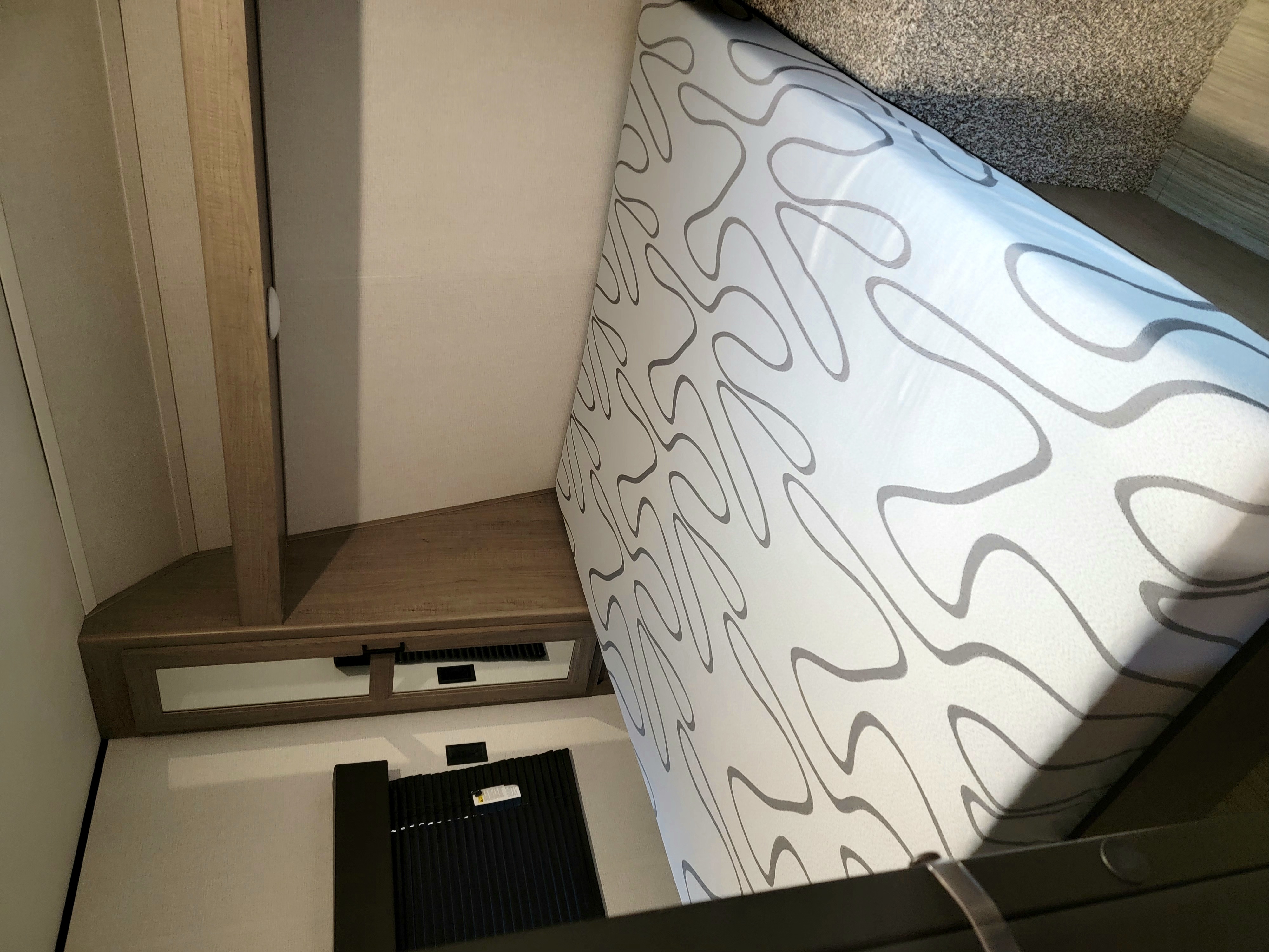 Interior view of an RV rental bedroom, featuring a patterned mattress, wooden nightstand with mirrored storage, and floor.. Keystone Hideout 2021