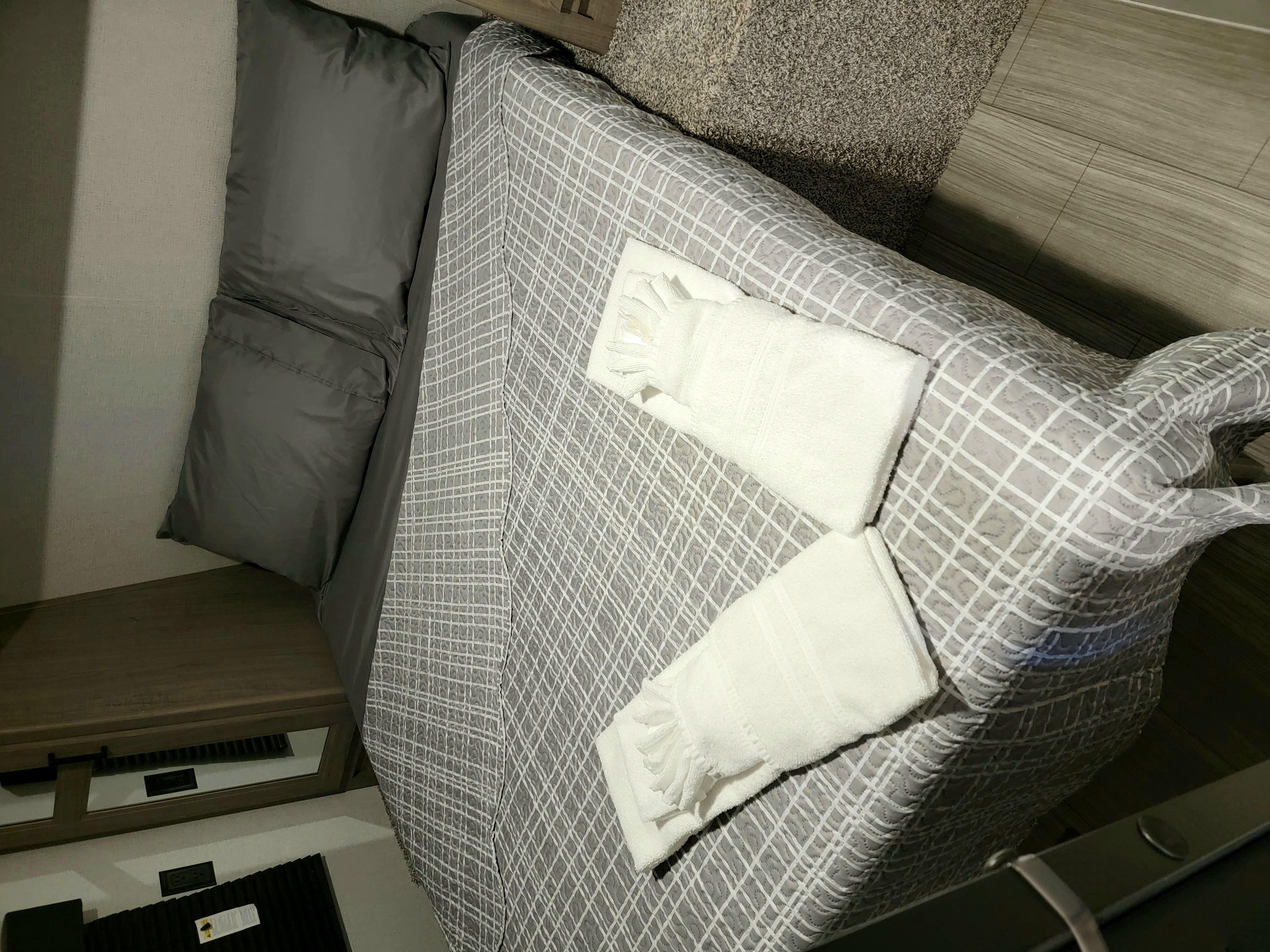 Cozy RV rental bedroom featuring neatly folded fresh towels on patterned bedding, a nightstand, and wood-look flooring.. Keystone RV Hideout 2021
