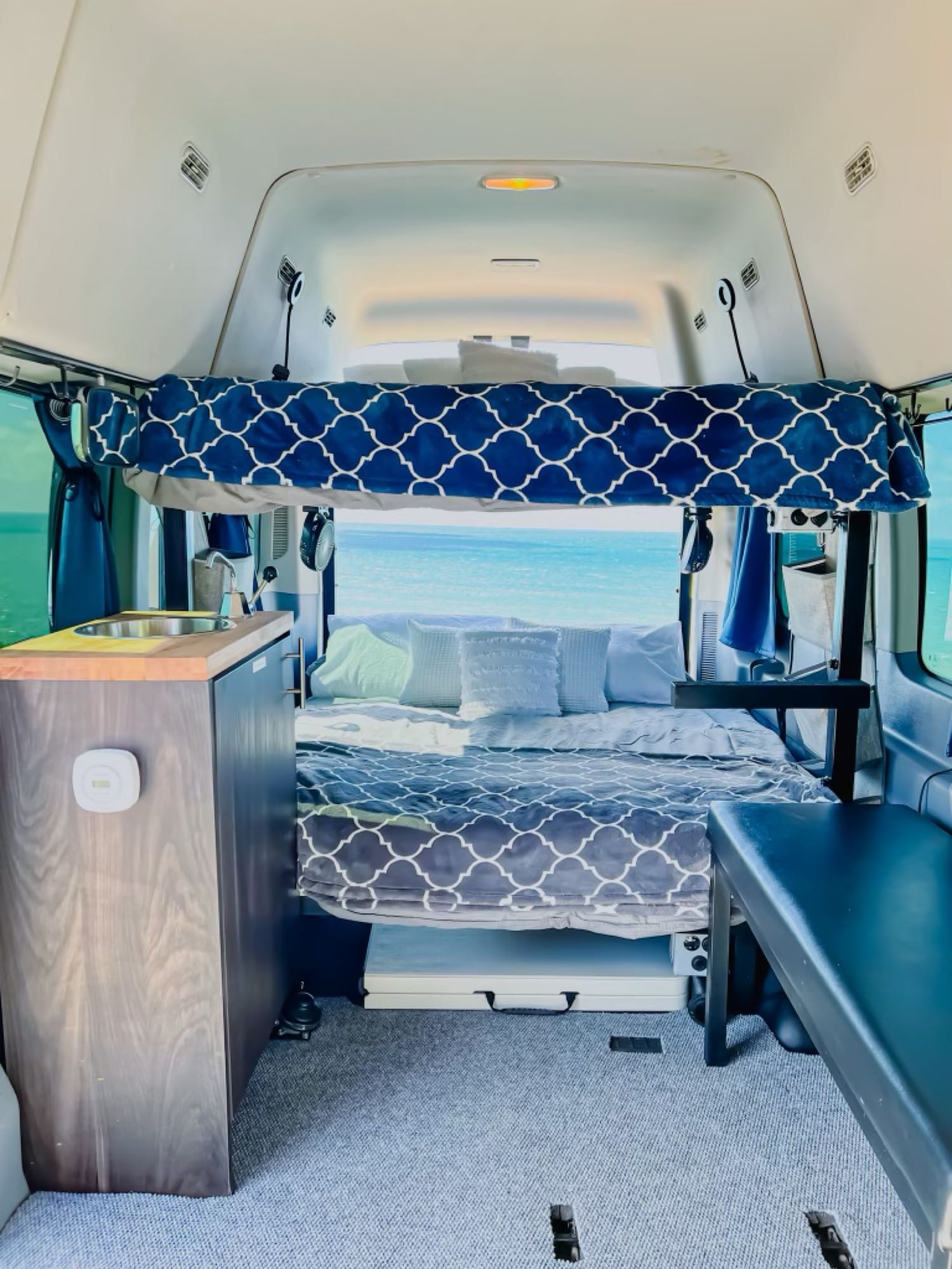 Cozy rv rental interior with a comfy bed, compact kitchen on left, and stunning ocean view out the back. Ideal for van life.. Ford Transit Custom 2019