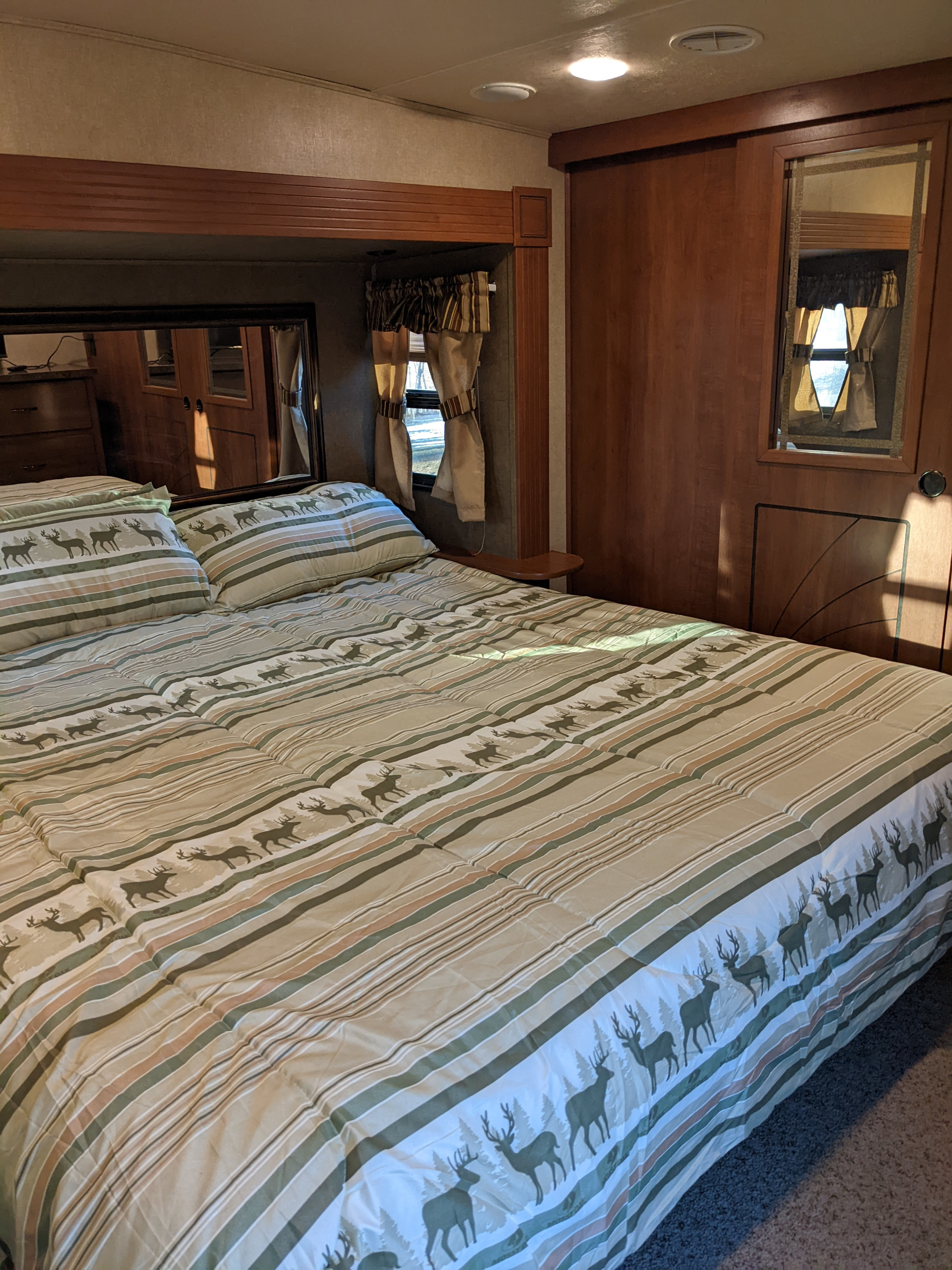 Cozy RV rental bedroom features a bed with deer-patterned bedding, wood accents, and a compact layout.. Forest River Sandpiper 2015