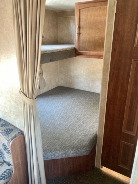 RV rental: Interior view of upper and lower bunk beds with grey cushions, a wood cabinet, and a beige curtain.. Jayco Jay Feather 2011