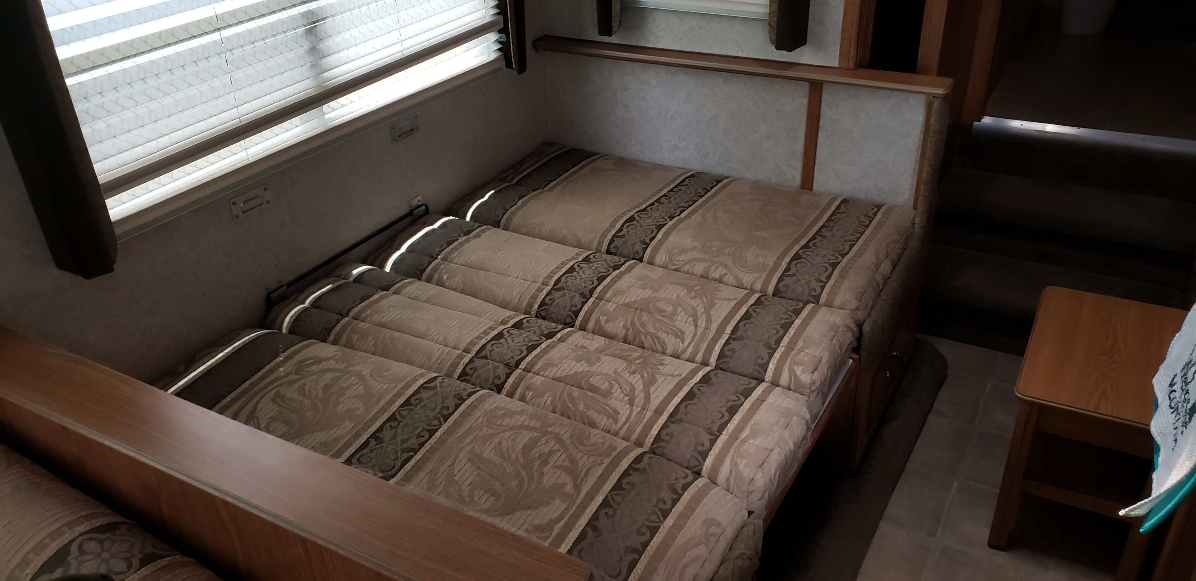 Cozy RV rental interior with a patterned fold-out sofa bed, windows with blinds, and a small wooden table.. Glendale Titanium 2004