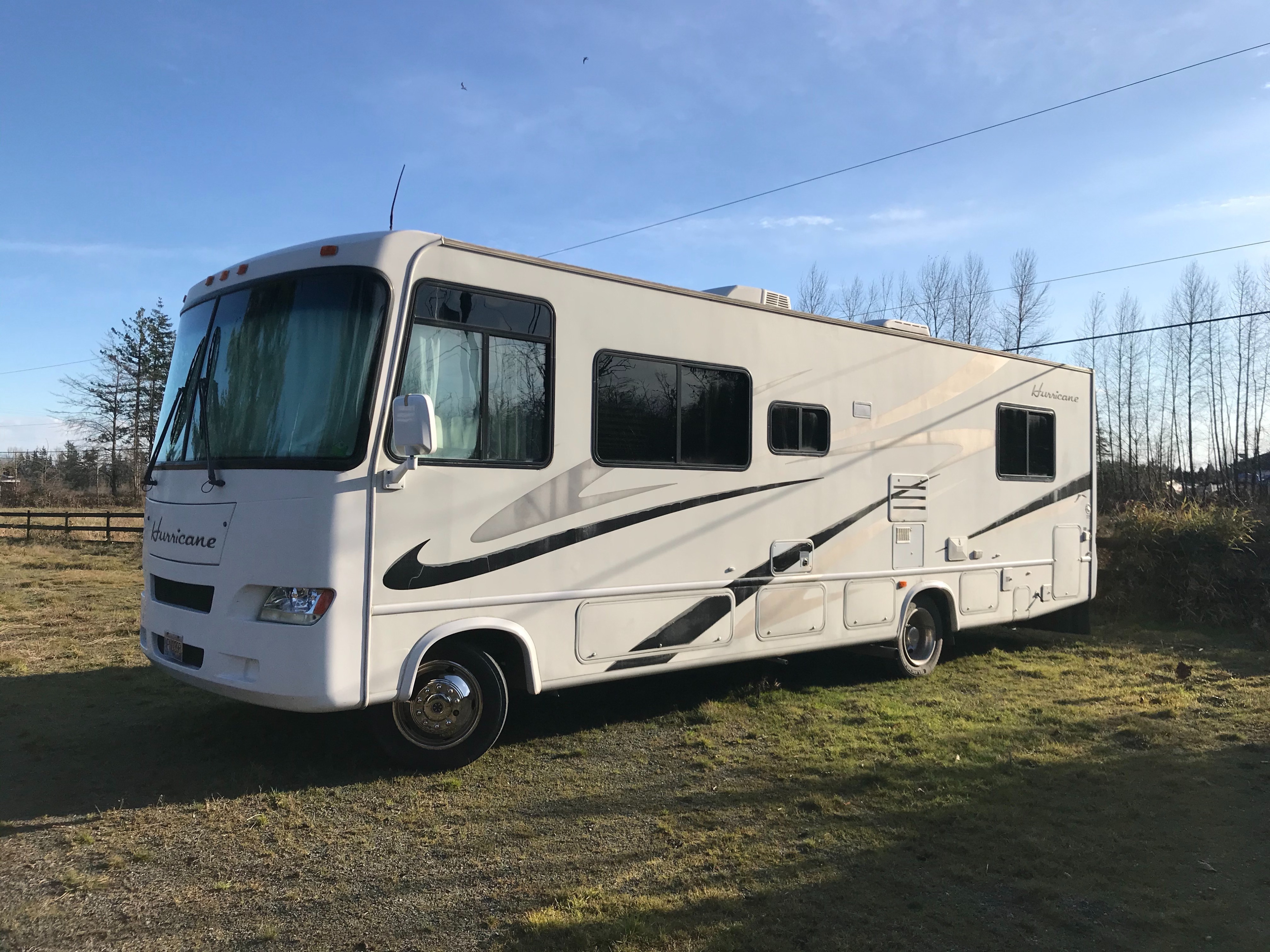 Explore travel with this white Hurricane RV motorhome rental, parked in a grassy field under a clear sky.. Thor Motor Coach Hurricane 2006
