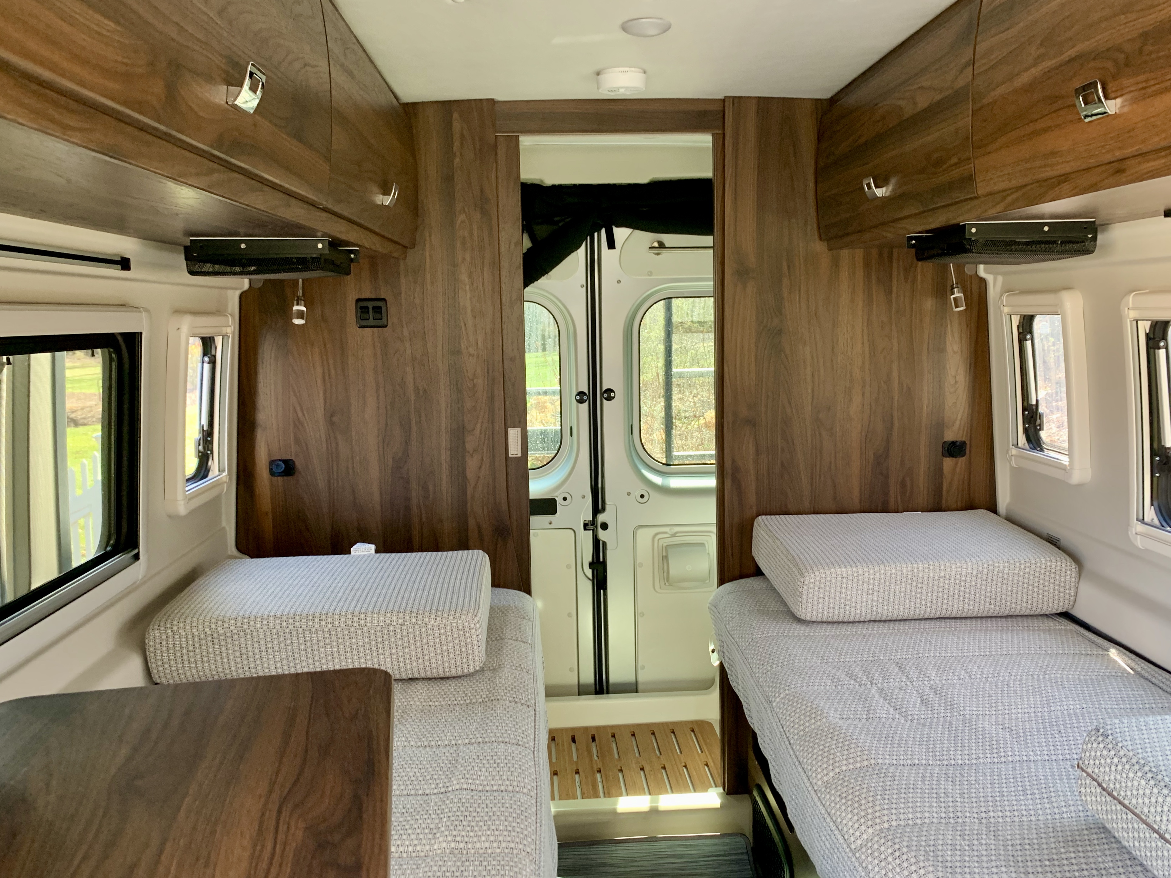 Cozy RV rental interior with two beds, overhead cabinets, and wood accents, perfect for a road trip.. Winnebago Travato 2022