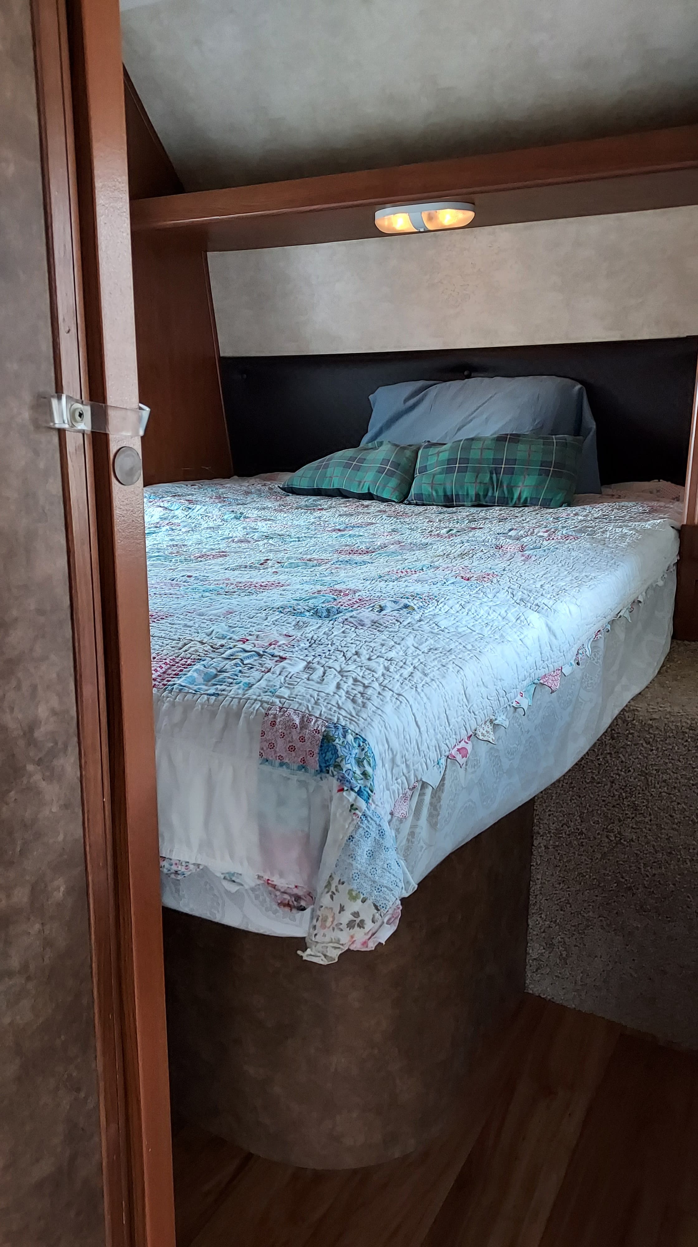 Compact RV rental bedroom featuring a cozy bed with a colorful quilt and an overhead light.. Forest River Wildwood 28 DBUD 2014
