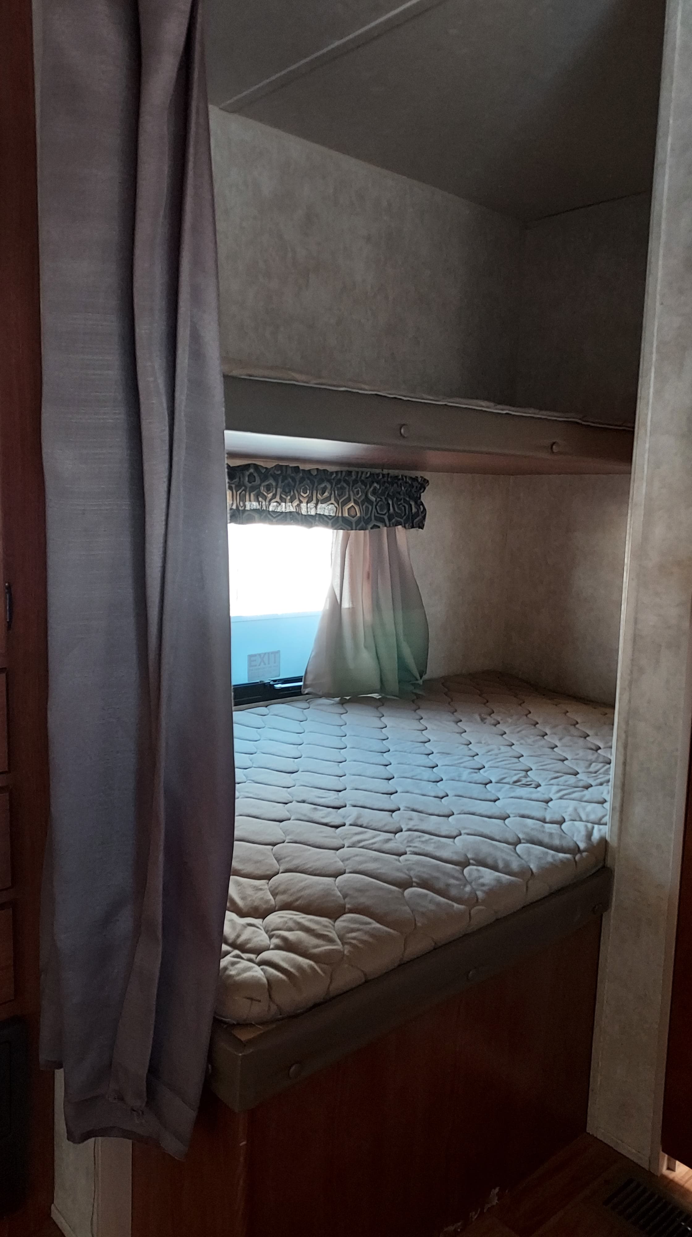 Cozy RV rental bunk bed with a quilted mattress, privacy curtain, and bright window, ready for rest.. Forest River Wildwood 28 DBUD 2014